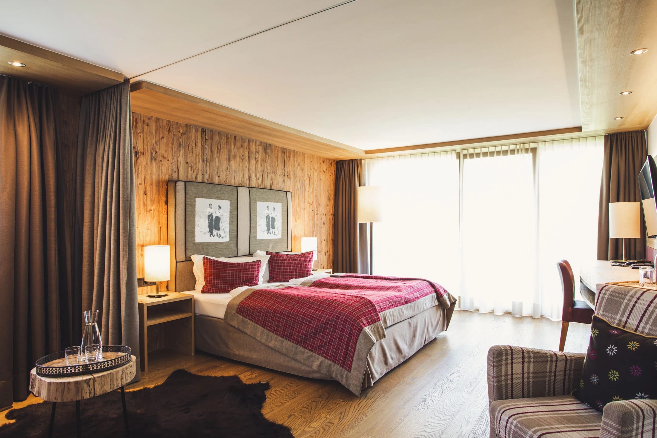 Hotelzimmer mit Doppelbett und roter Tagesdecke, Holzwand, Schreibtisch und Sesseln
