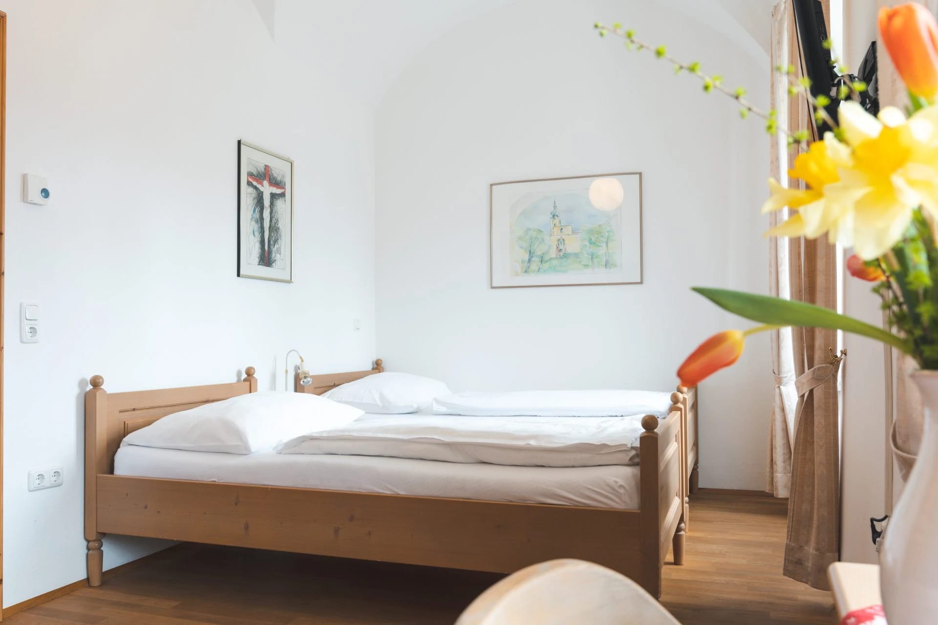 Helles Zimmer mit hölzernem Doppelbett vor weiß gewölbter Wand und Bildern an der Wand