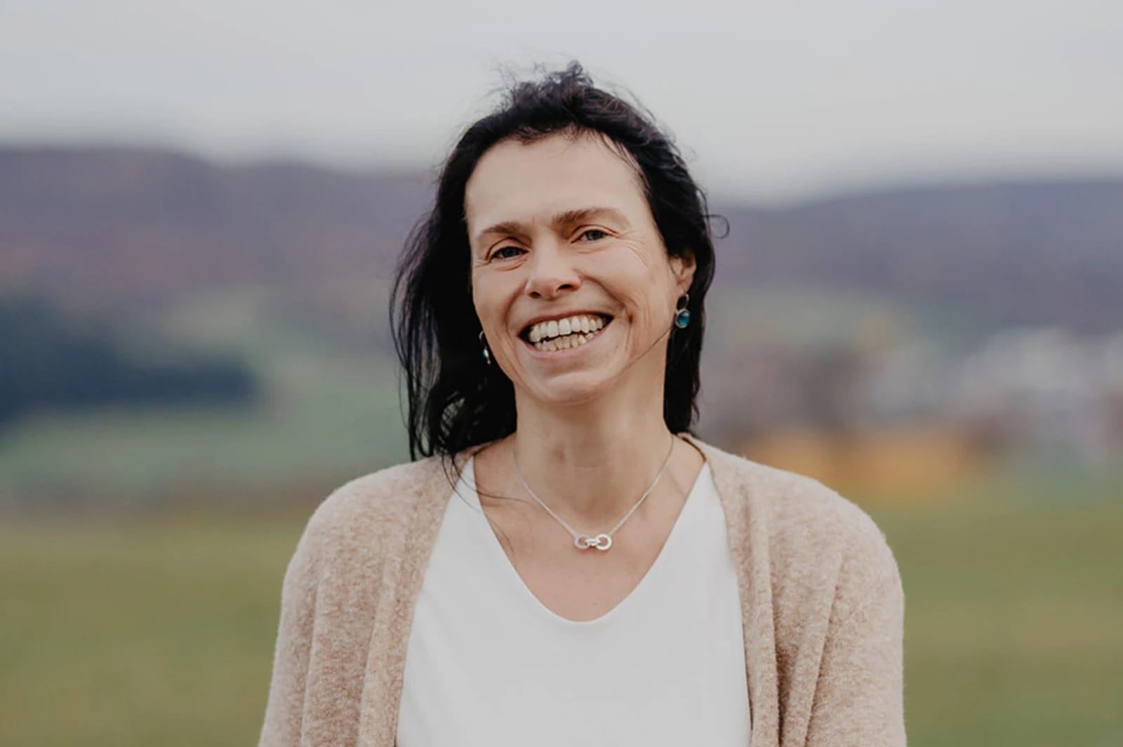 Porträt von Sabine Czilwa, lächelnd im Freien mit Hügellandschaft im Hintergrund