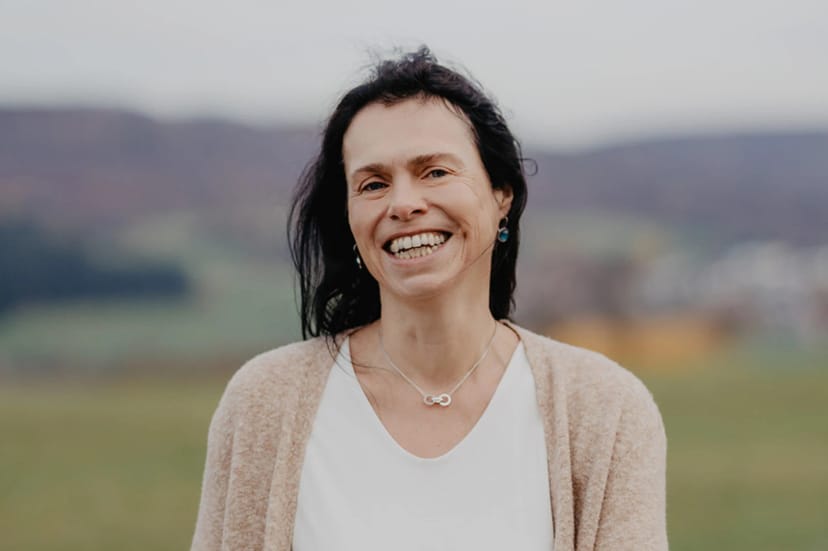 Porträt von Sabine Czilwa, lächelnd im Freien mit Hügellandschaft im Hintergrund
