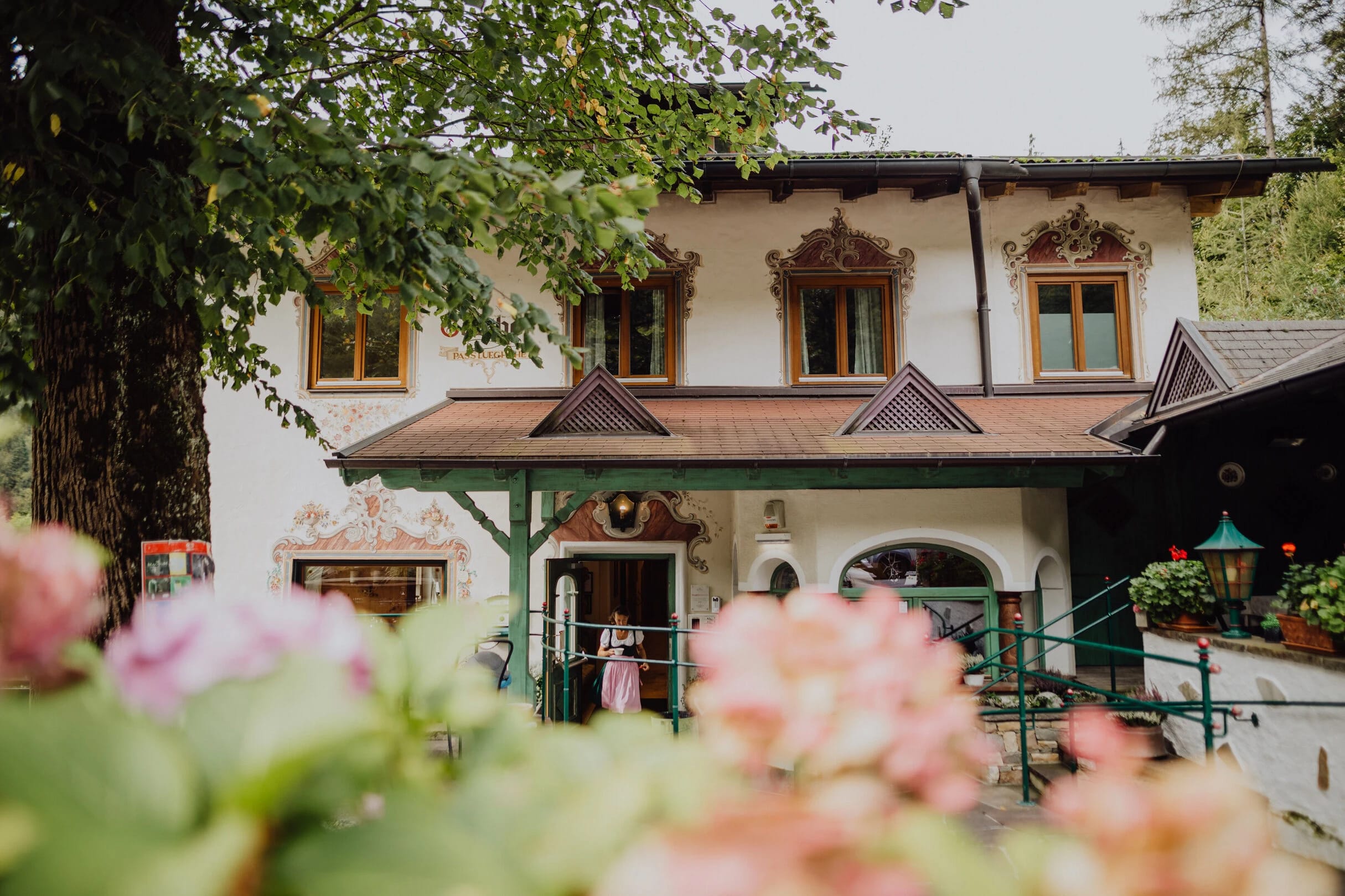 Außenansicht des traditionellen Alpenhauses mit bemalter Fassade, Giebeldach und Blumen im Vordergrund