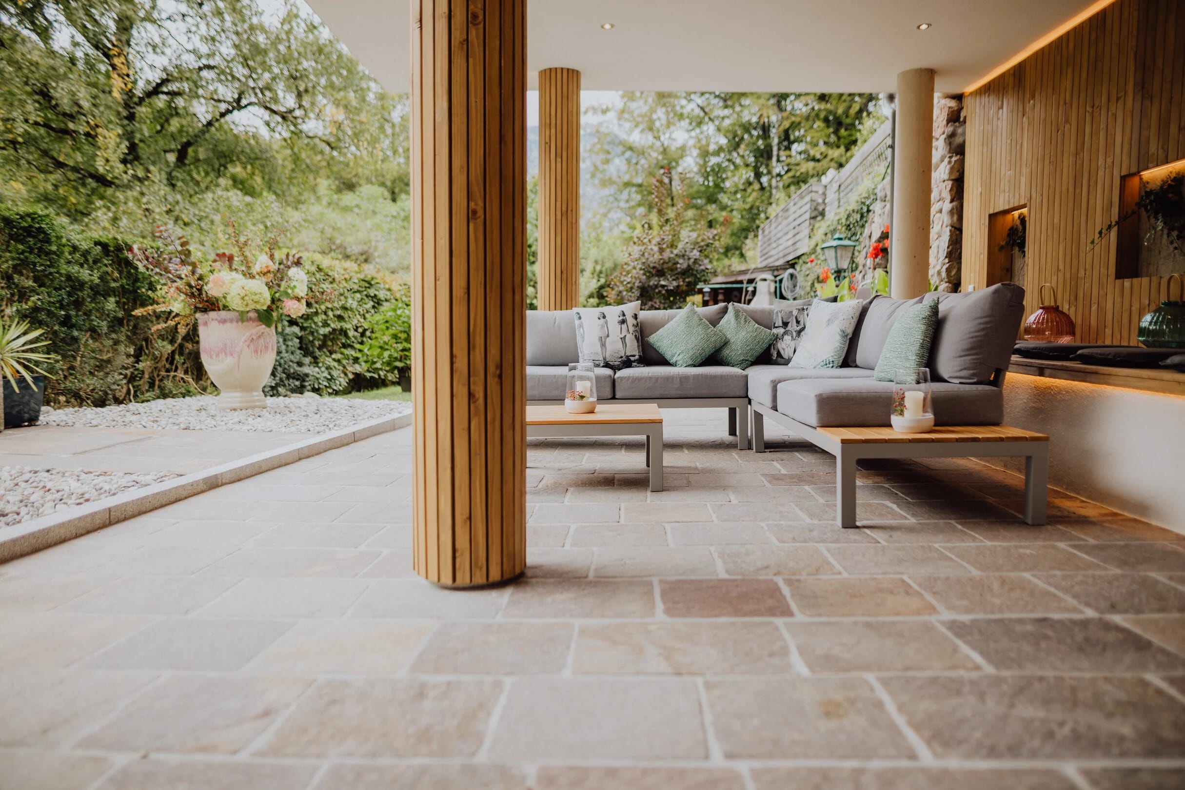 Überdachte Terrassenlounge mit Polstersofas auf Natursteinboden und Blick in den Garten