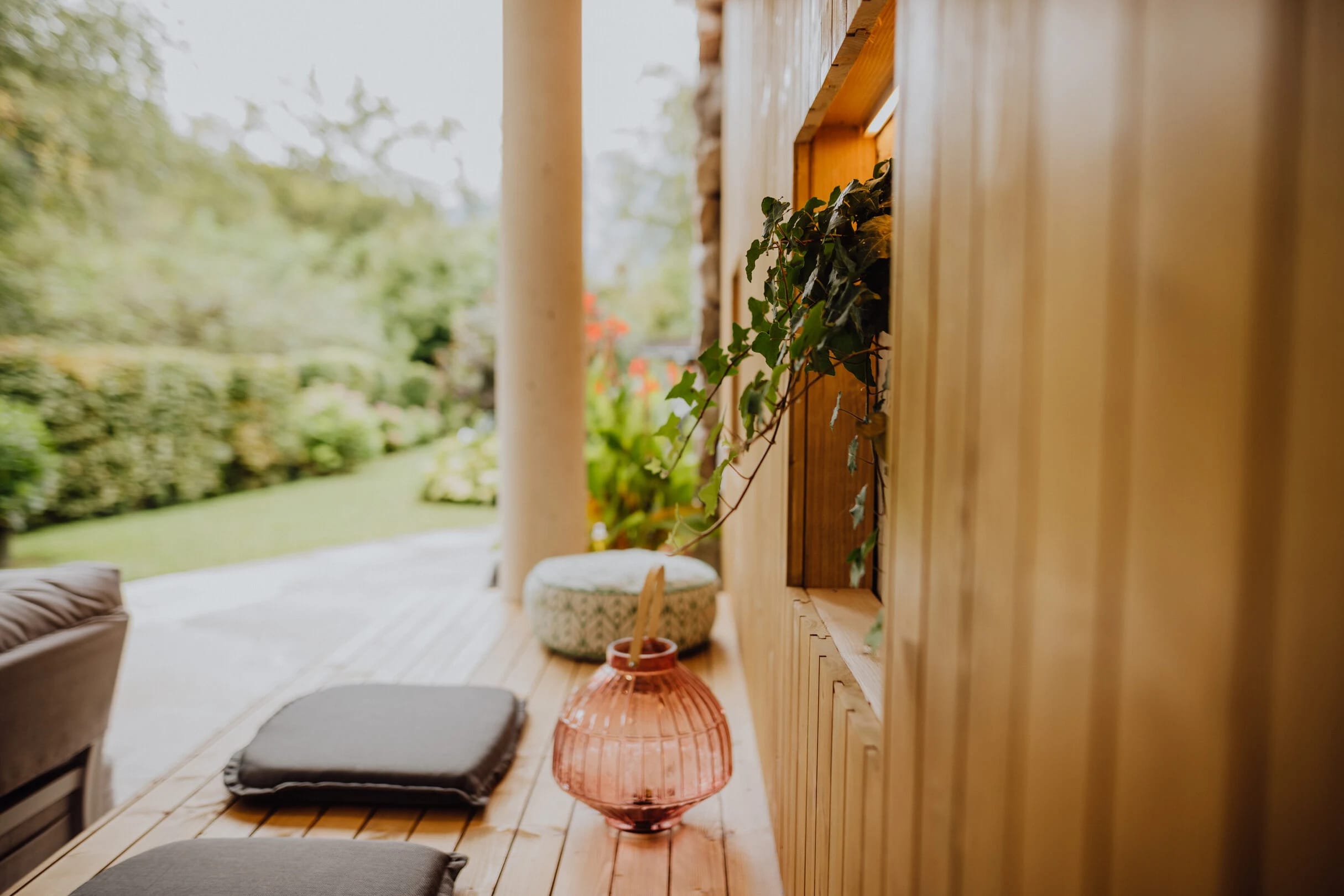 Überdachte Holzveranda mit Sitzkissen und Blick in den bepflanzten Garten
