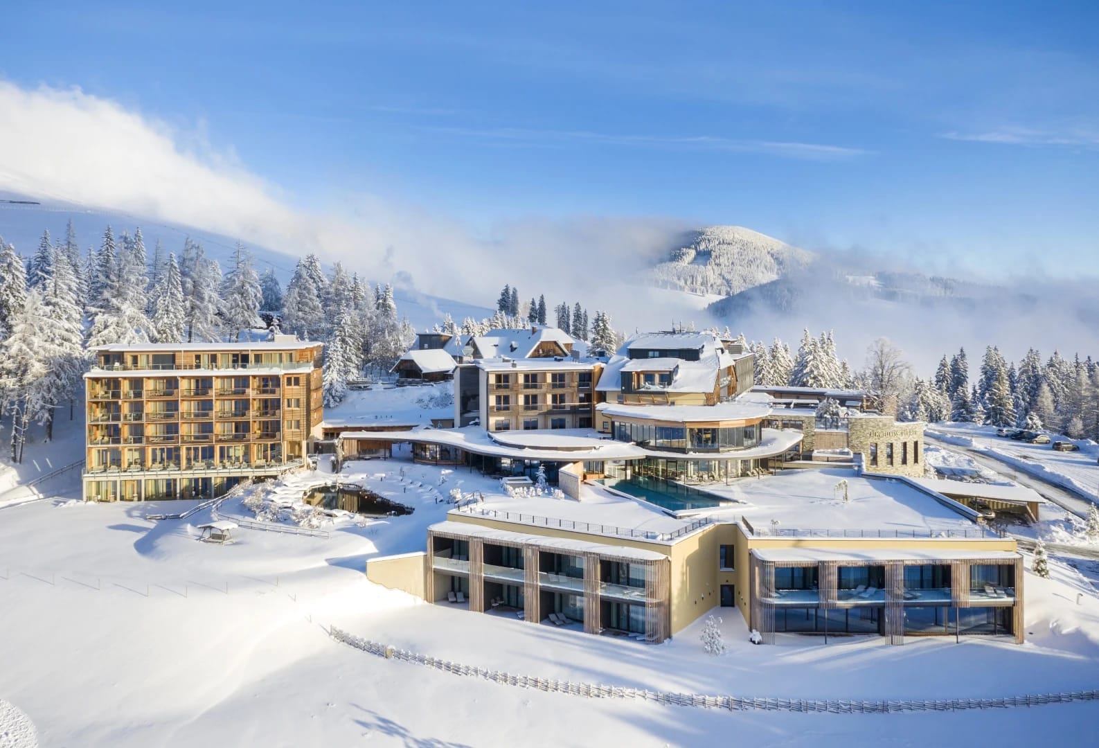Verschneite Außenansicht der Hotelgebäude mit Bergkuppe und Nebel im Hintergrund