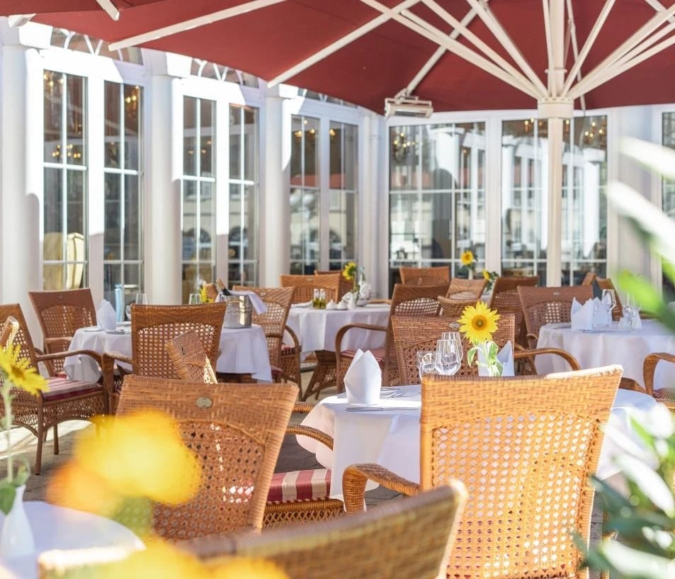 Überdachte Terrasse mit Korbstühlen, eingedeckten Tischen und Sonnenschirmen