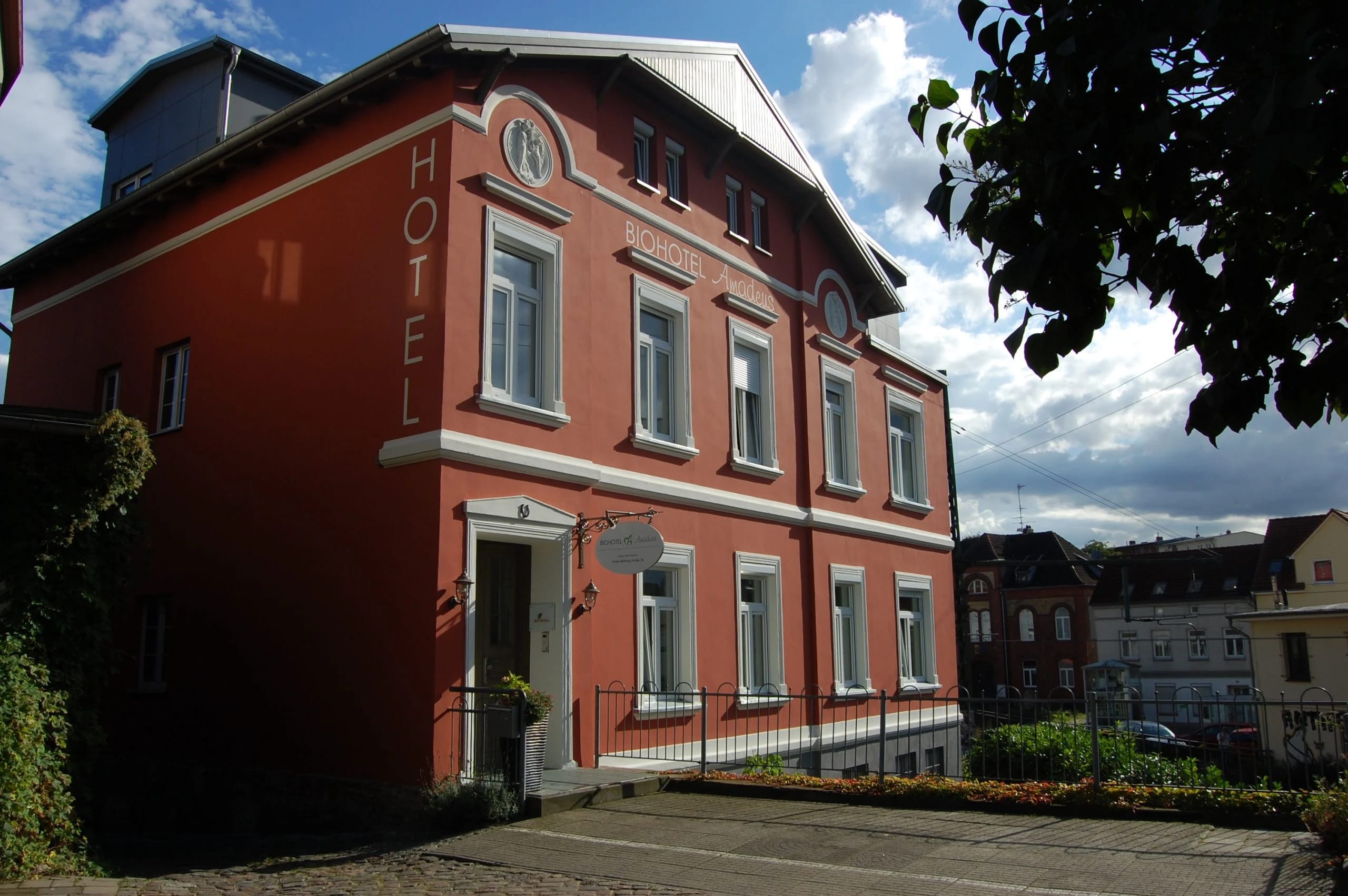 Rotes Hotelgebäude mit weißen Fensterrahmen und senkrechtem HOTEL-Schriftzug unter blauem Himmel