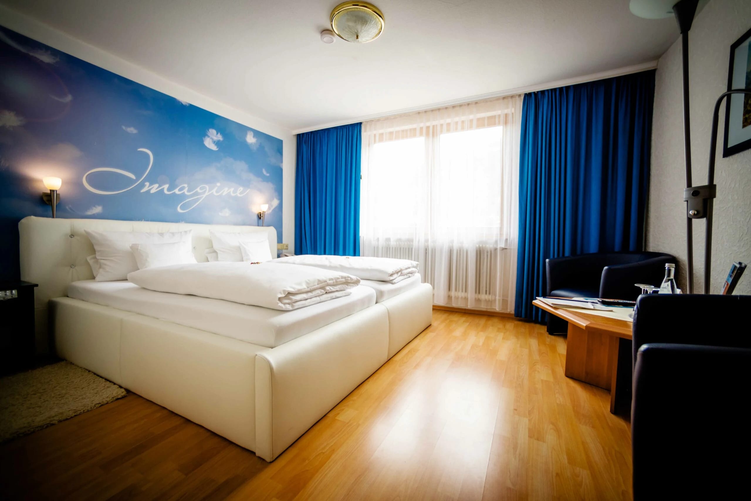 Modernes Doppelzimmer mit weißem Polsterbett, blauen Vorhängen und Wandbild hinter dem Bett