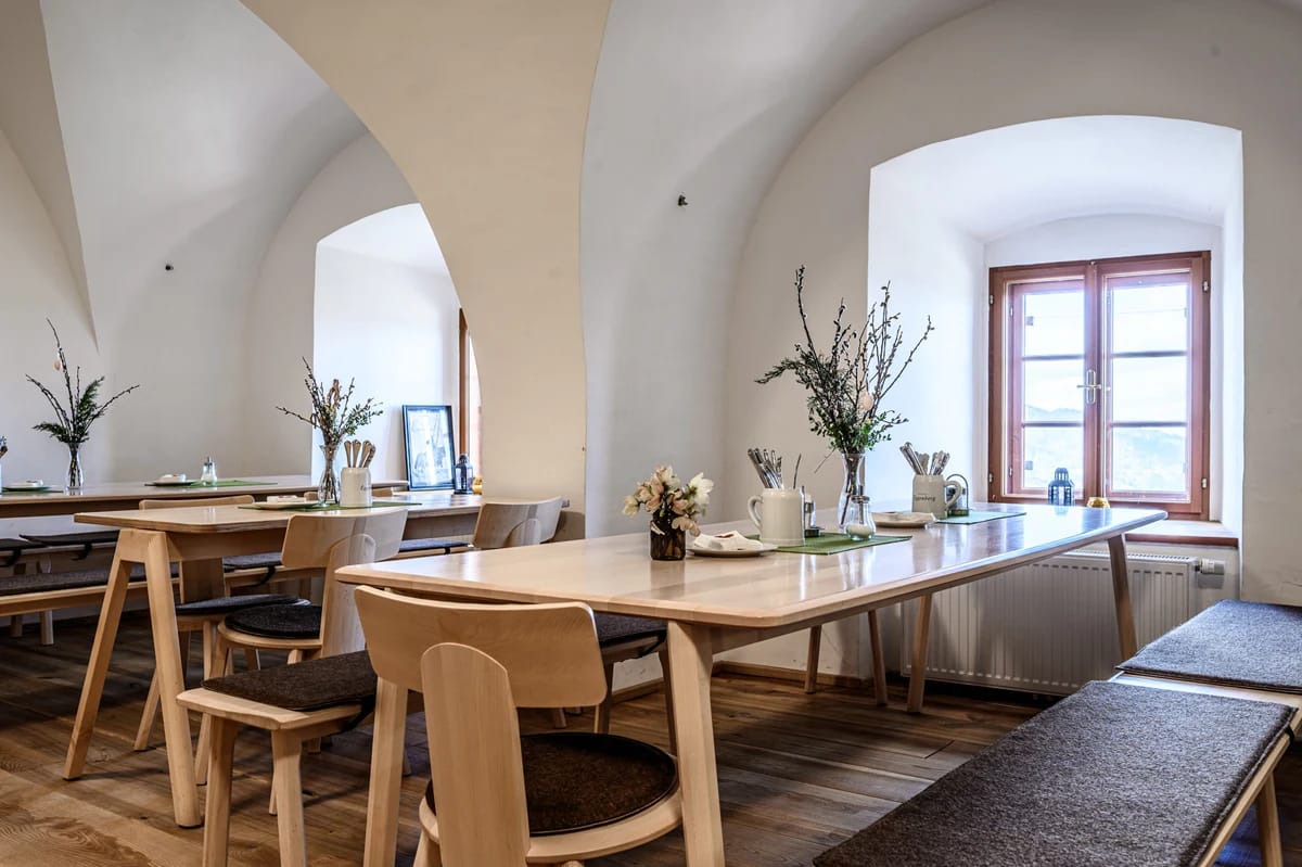 Gewölbter Speiseraum mit hellen Holztischen, Bänken und Fensternische