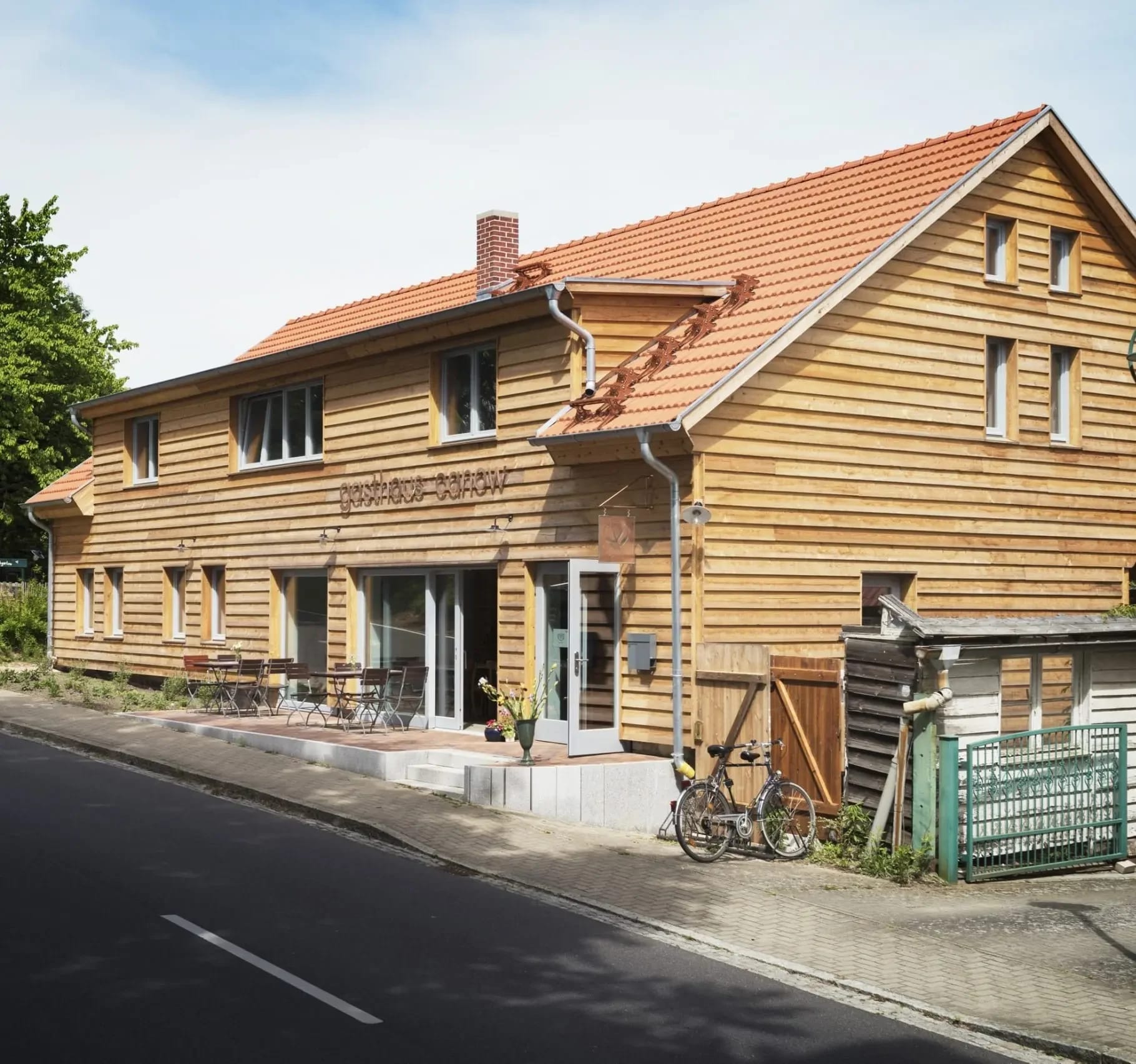 Außenansicht des Gasthauses mit Holzfassade, rotem Ziegeldach und Terrasse an der Straße