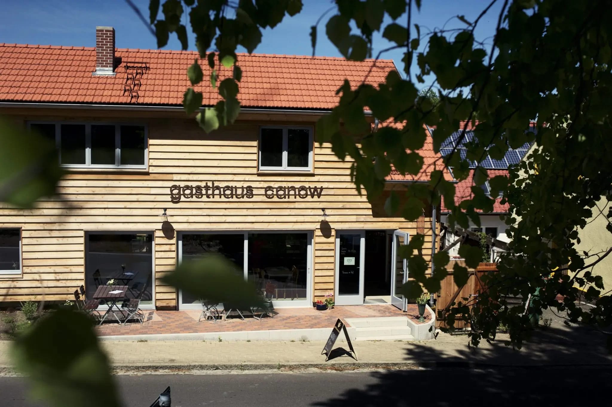Vorderansicht des Gasthaus Canow mit Holzfassade und Schriftzug, durch Bäume gesehen