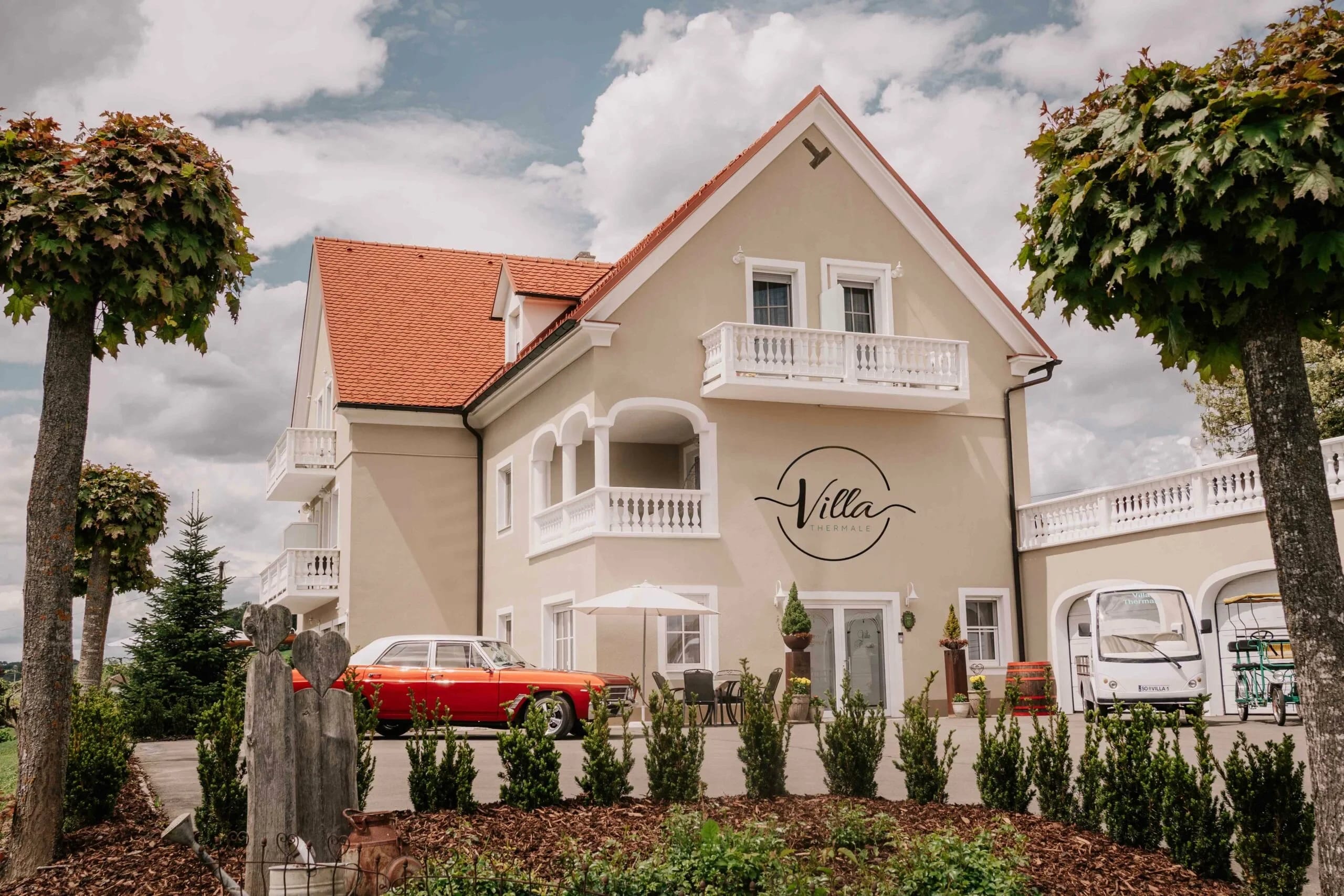 Cremefarbene Villa mit rotem Ziegeldach, Balkonen und Oldtimer vor dem Haus