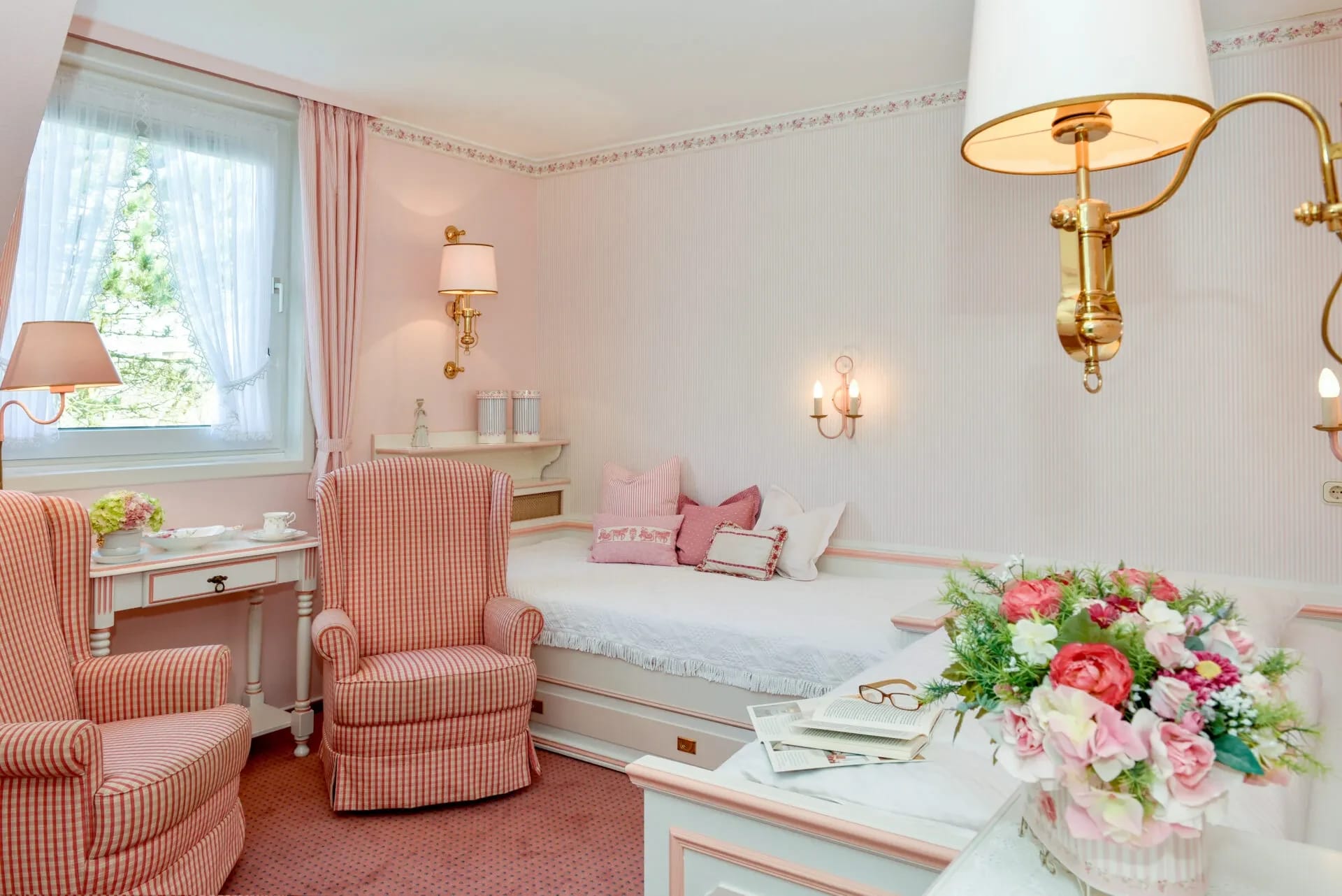 Sitzecke eines Zimmers in Rosétönen mit gestreiften Ohrensesseln und Blumenschmuck