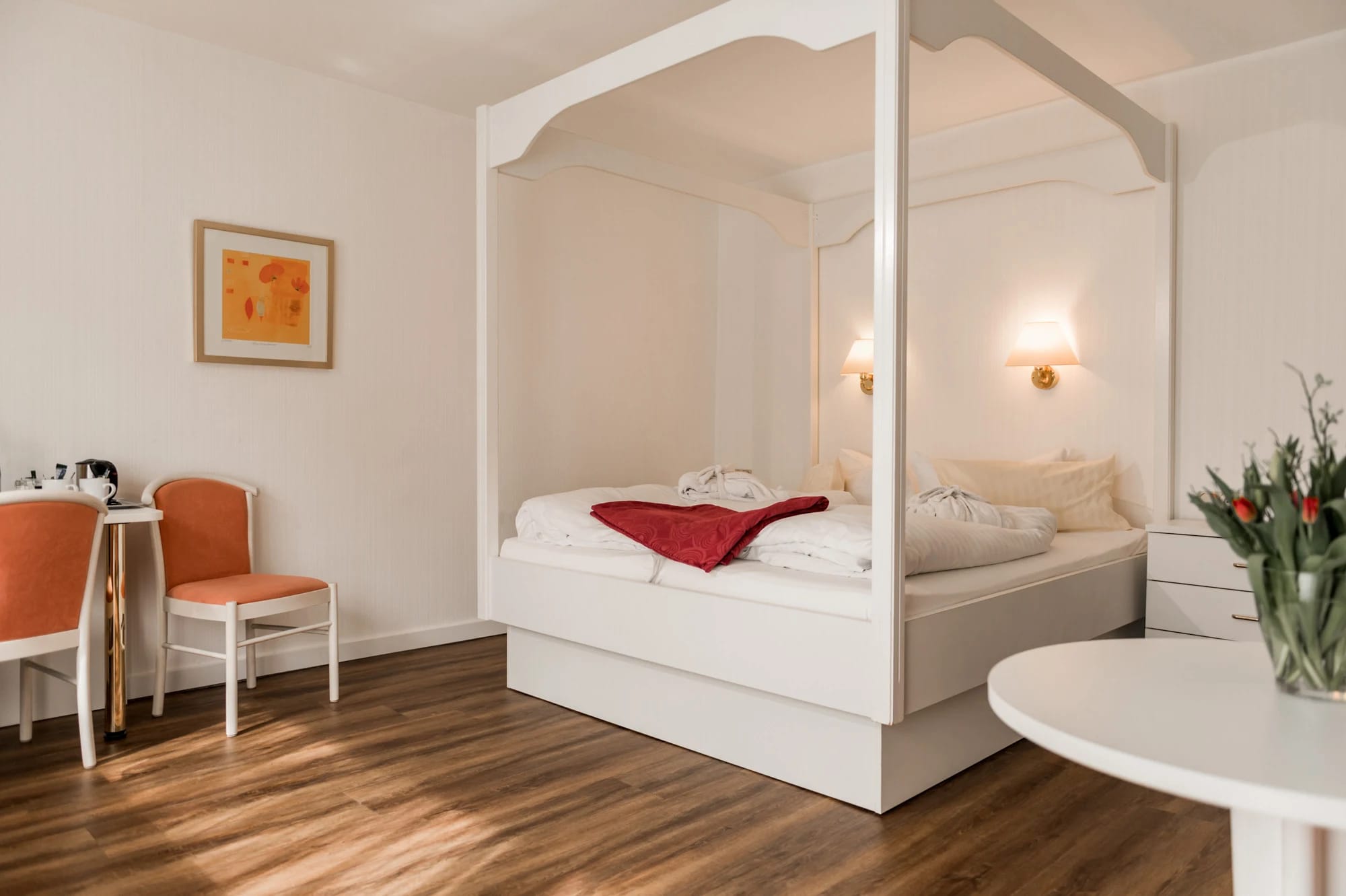 Zimmer mit weißem Himmelbett, kleiner Sitzecke und Holzboden