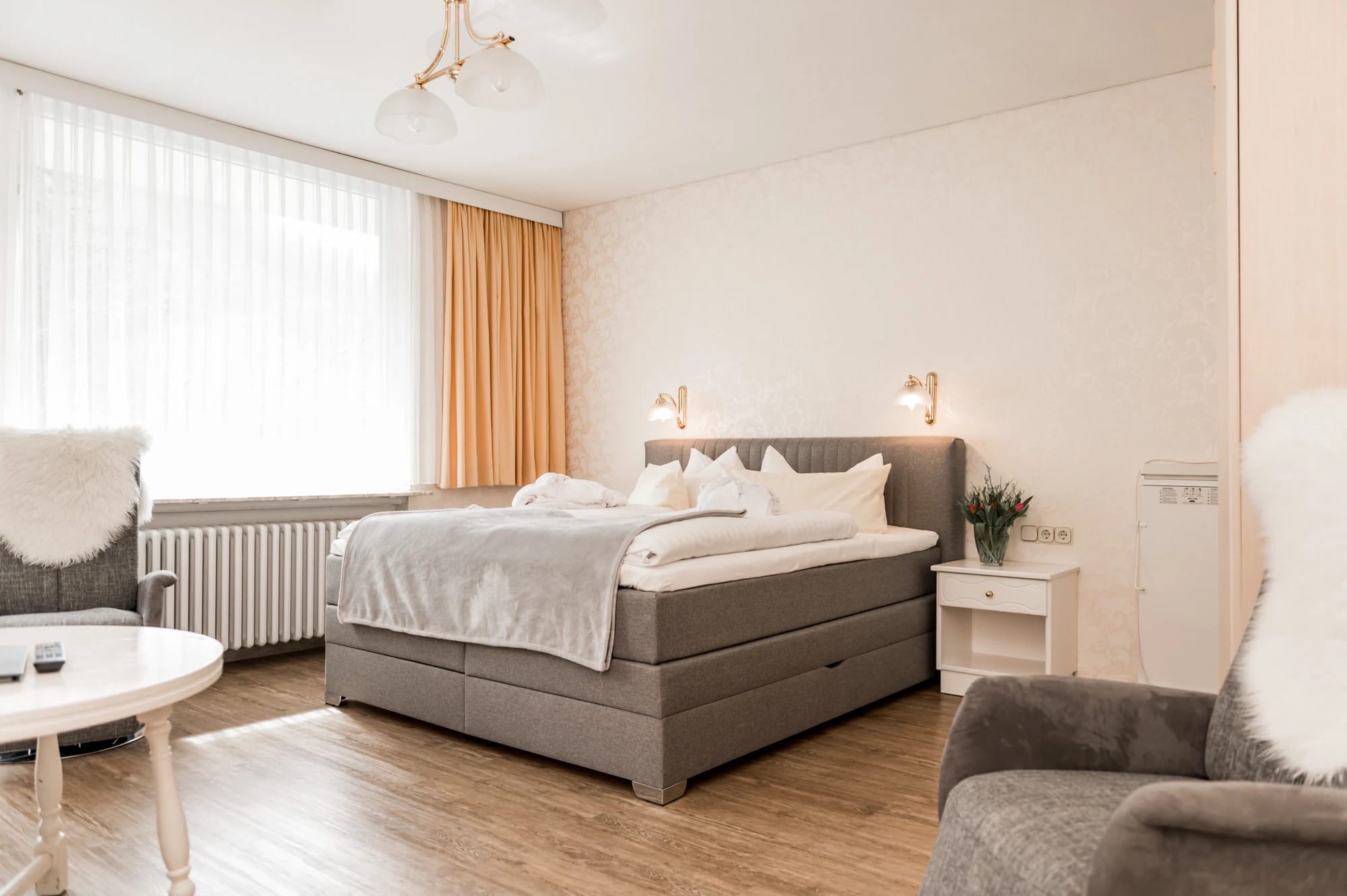 Helles Doppelzimmer mit Boxspringbett, Sessel mit Fell und Holzboden