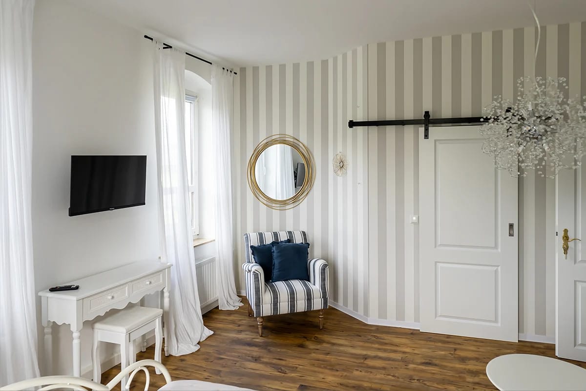 Zimmer mit gestreifter Wand, Sessel, Wandspiegel und weißem Schreibtisch
