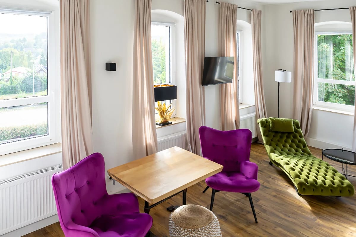 Helle Sitzecke mit lila Sesseln, grüner Chaiselongue und Fensterblick ins Tal