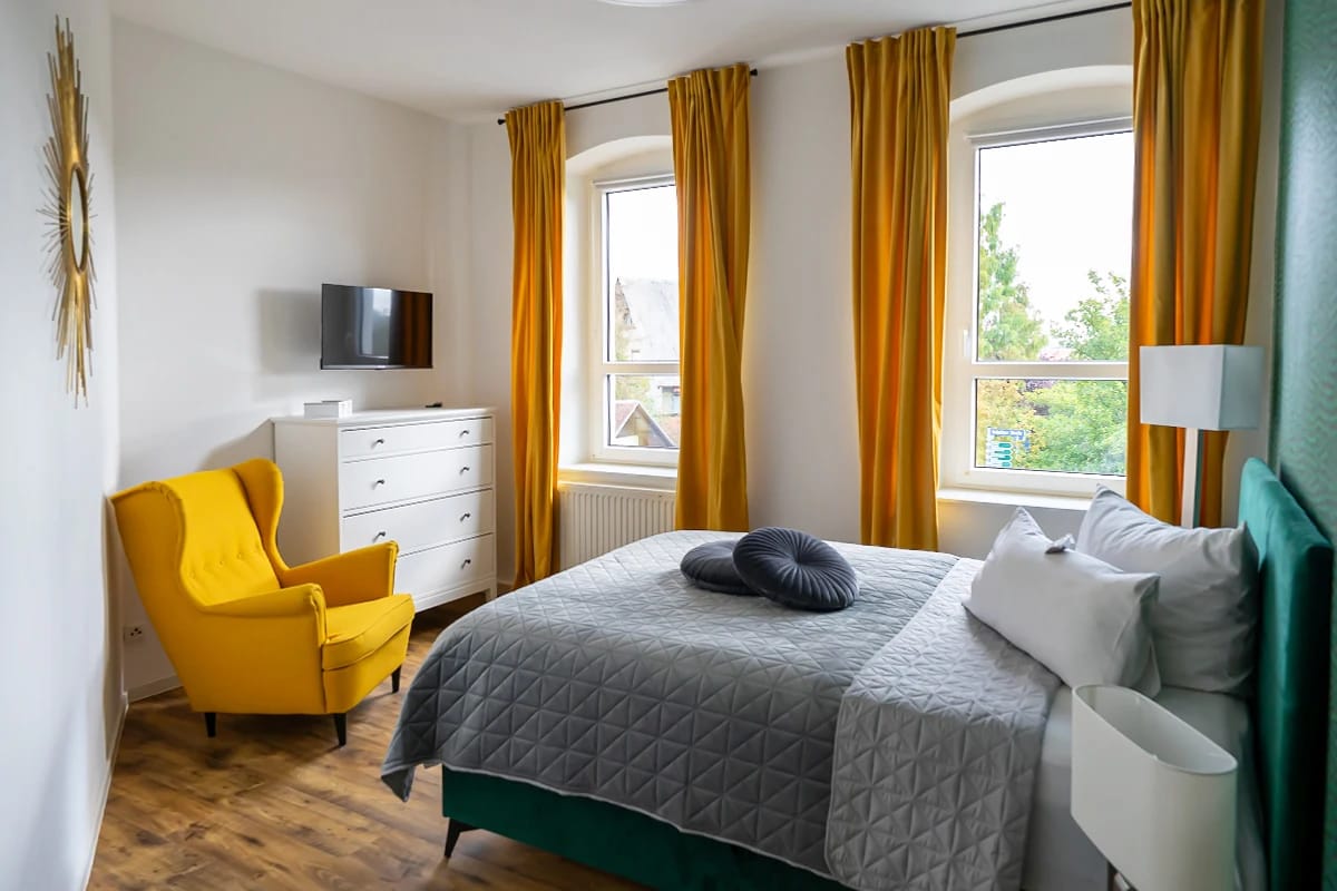 Zimmer mit gelbem Sessel, gelben Vorhängen und zwei Fenstern