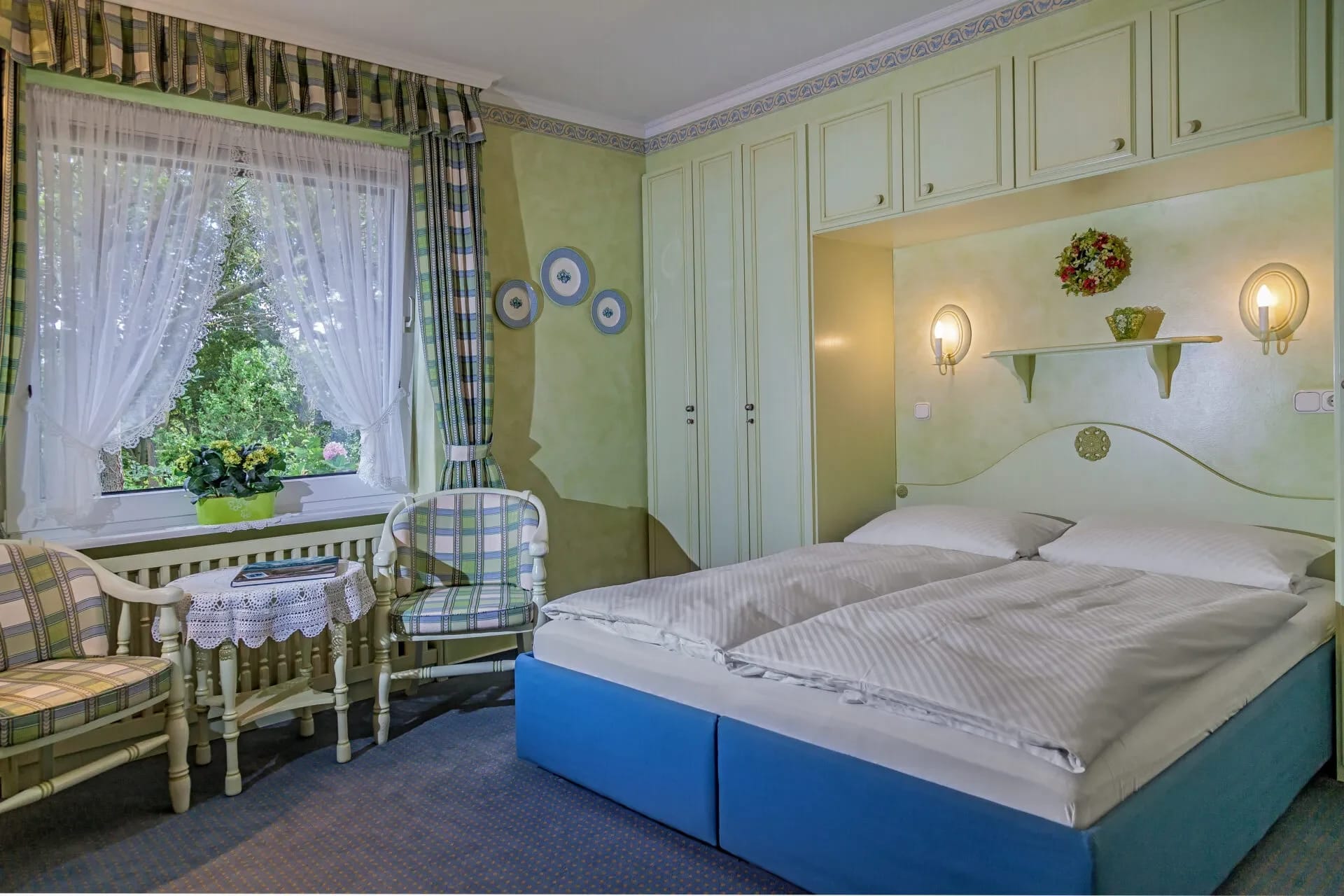 Gemütliches Doppelzimmer in Grüntönen mit Doppelbett, Sitzecke und Fenster zum Garten