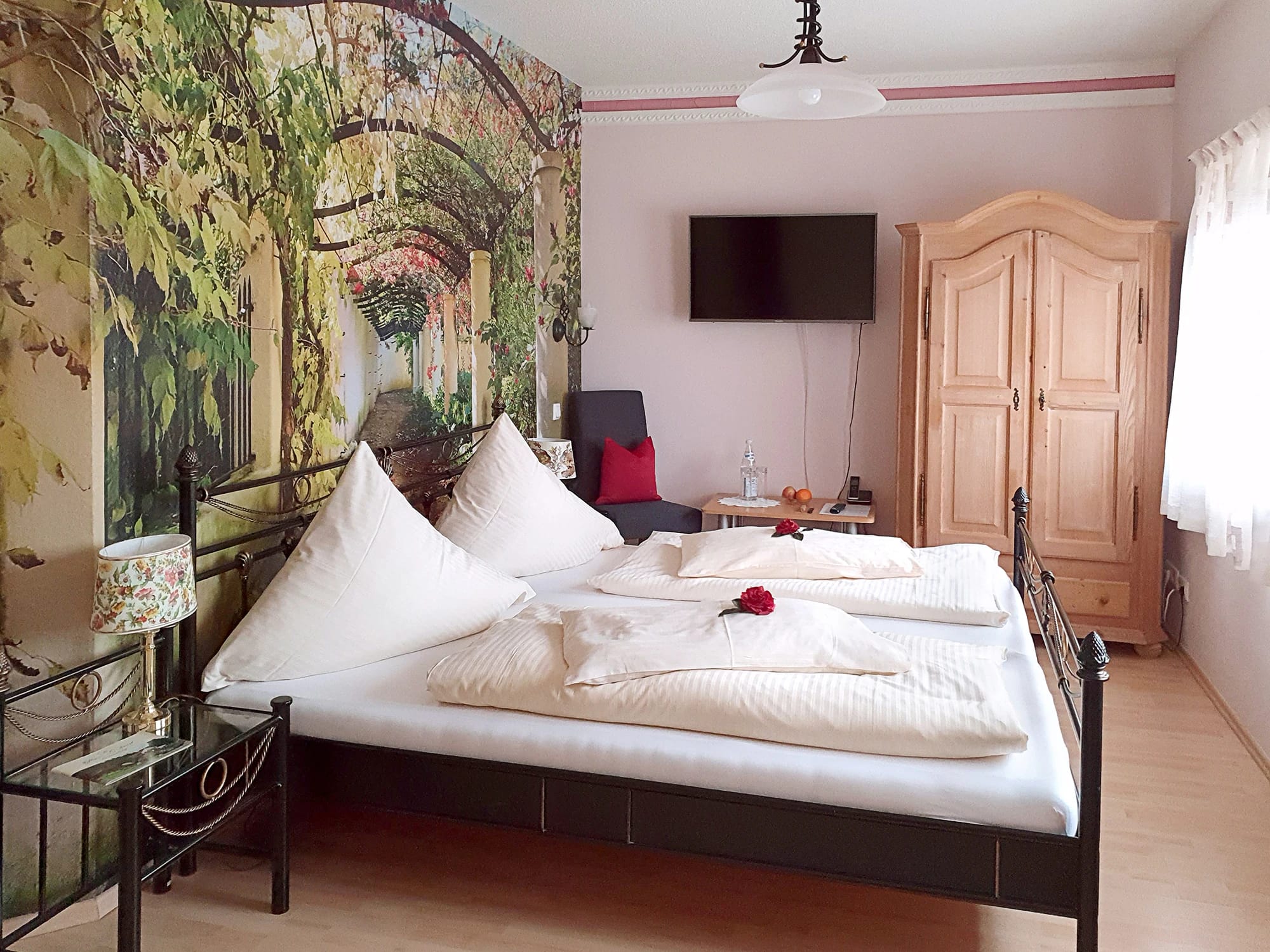 Doppelzimmer mit Doppelbett, Garten-Wandbild hinter dem Bett und Holzkleiderschrank