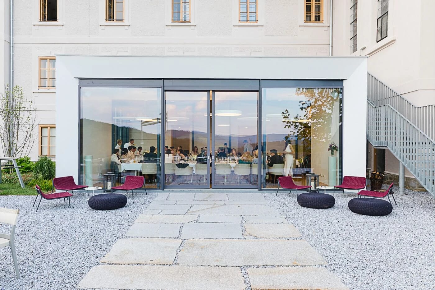 Verglaster Wintergarten mit Terrasse davor, Loungesessel und Sitzkissen auf Steinplatten