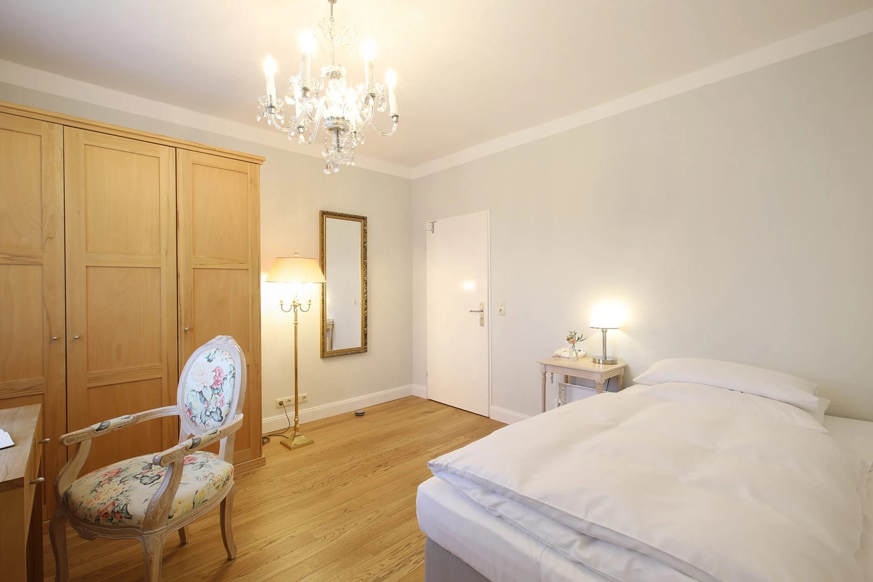Helles Zimmer mit Bett, Holzschrank und floralem Sessel