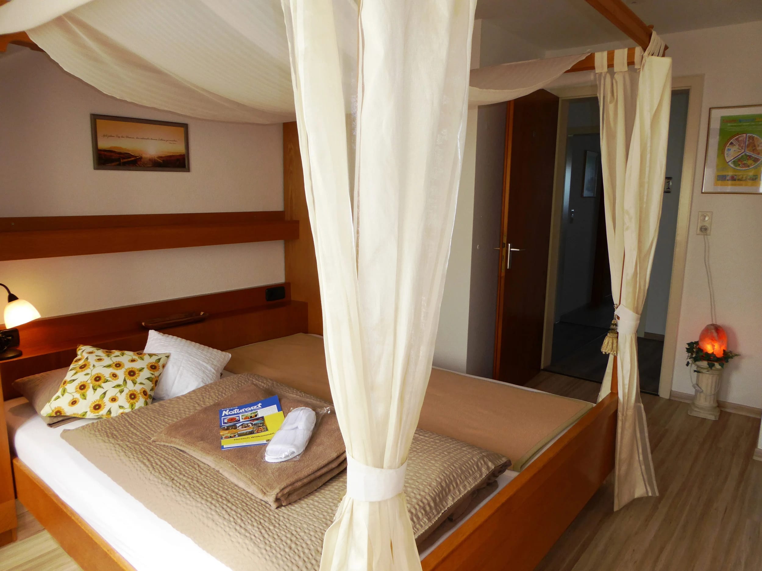 Zimmer mit Himmelbett und weißen Vorhängen, Holzboden und Salzlampe