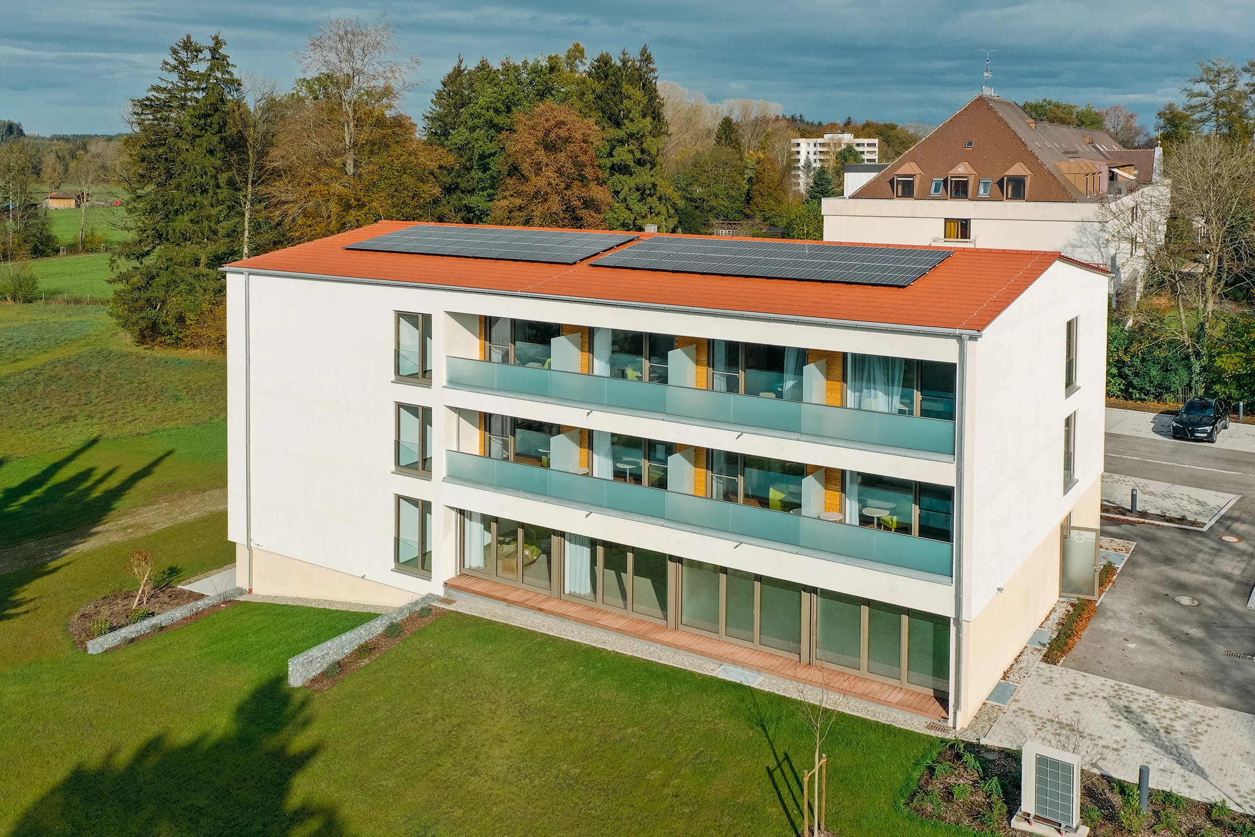 Gästehaus-Neubau mit Balkonen und rotem Solardach auf der Wiese
