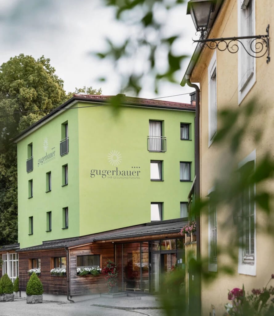 Hausfassade mit Schriftzug gugerbauer und überdachtem Eingang mit Blumenkästen
