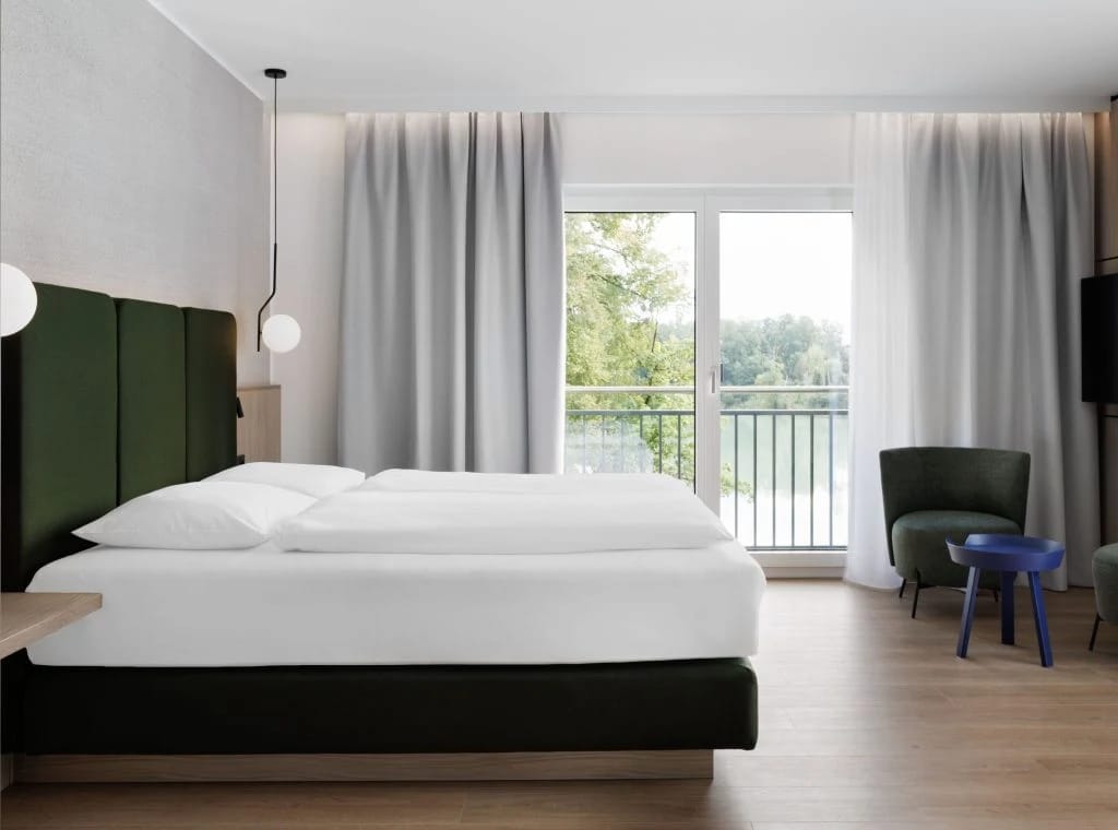 Doppelzimmer mit dunkelgrünem Polsterkopfteil, Sessel und Balkontür mit Blick ins Grüne