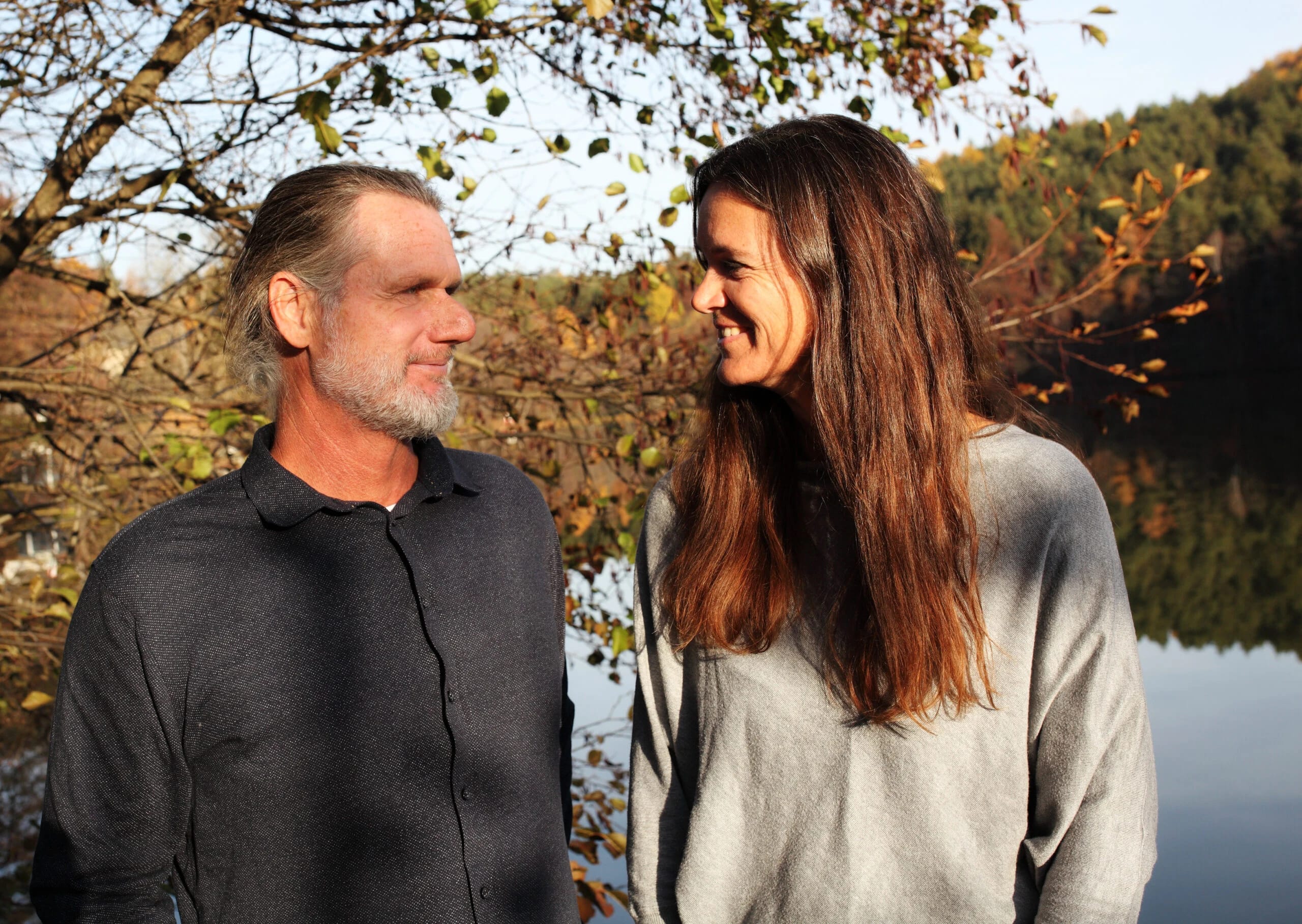 Heidi Allesch und Martin Weissböck lachen sich am Ufer des Weissensees im Herbstlaub an