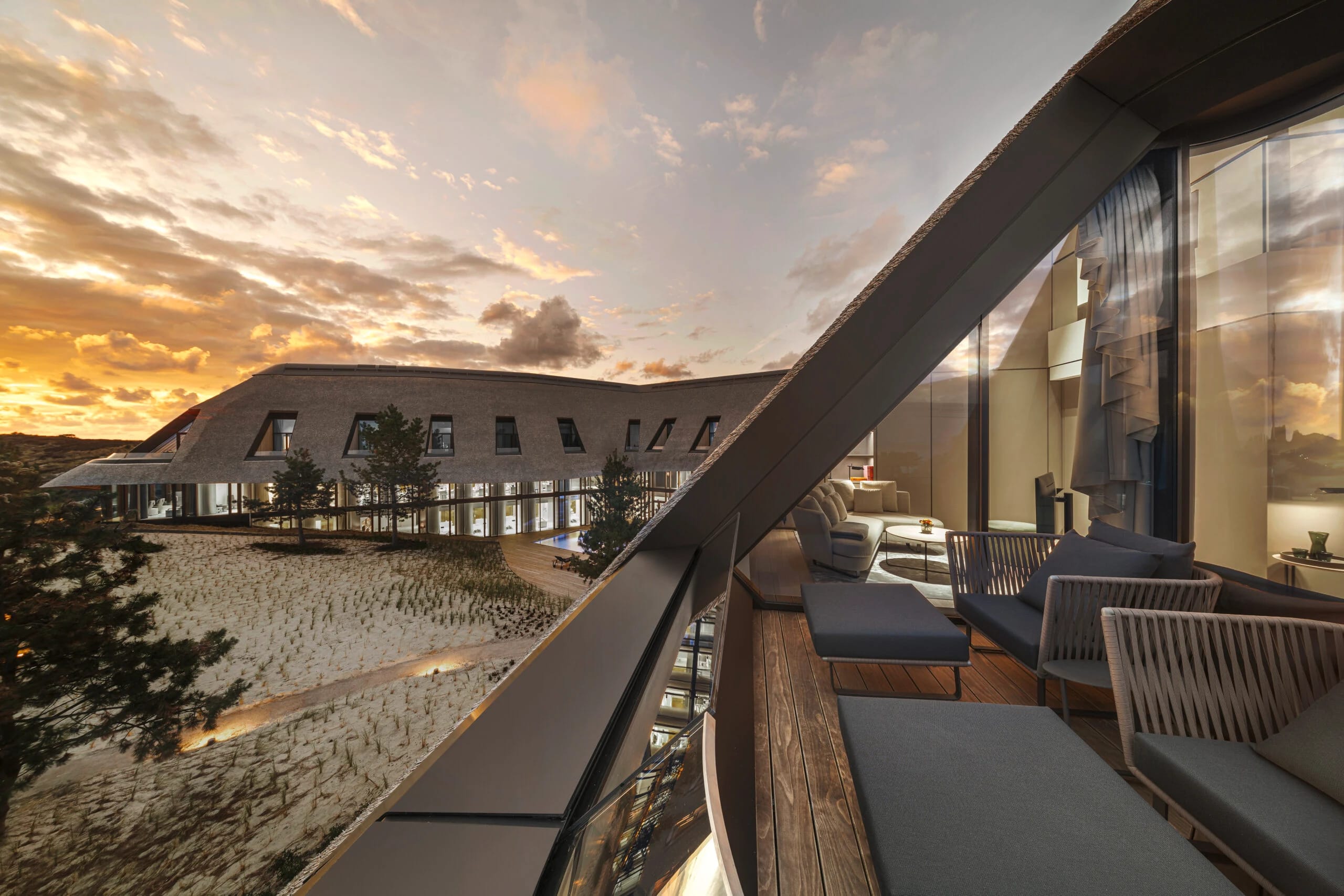 Terrasse mit Loungesesseln, dahinter das reetgedeckte Gebäude im Abendrot