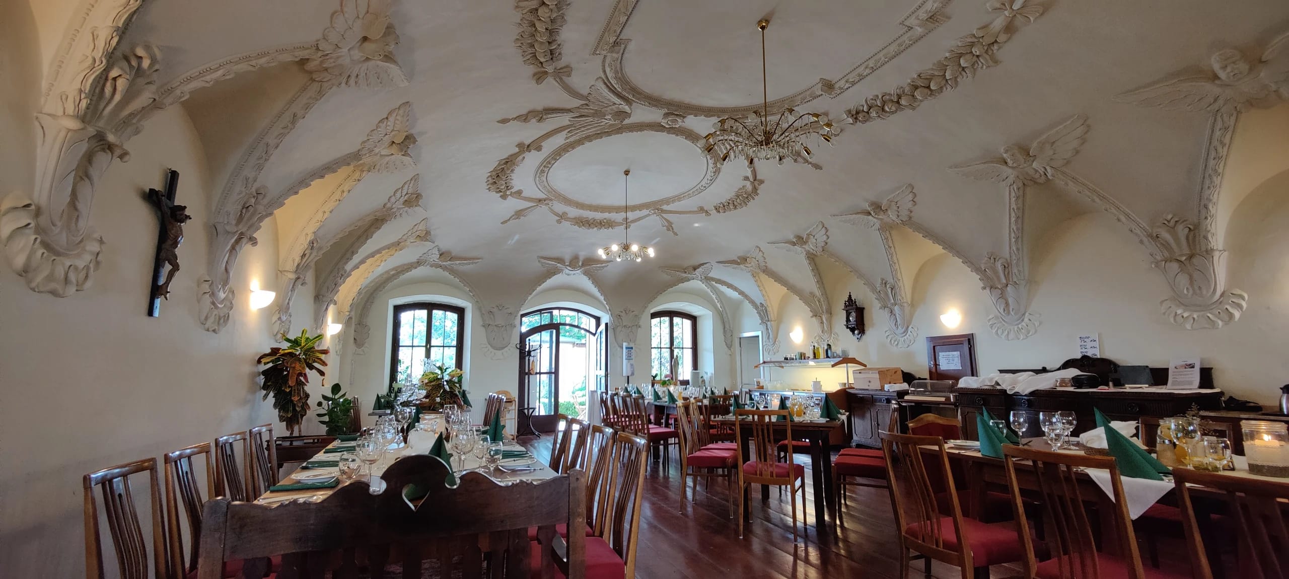 Saal mit reich verzierter weißer Stuckdecke, Luster und langen eingedeckten Tischen