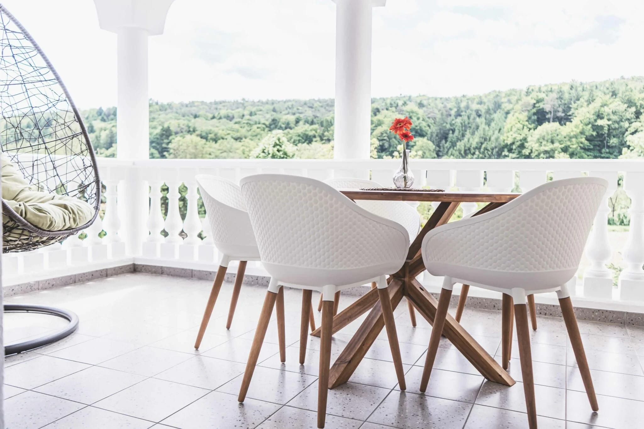 Überdachte Loggia mit weißen Stühlen, Hängesessel und Blick über den Wald