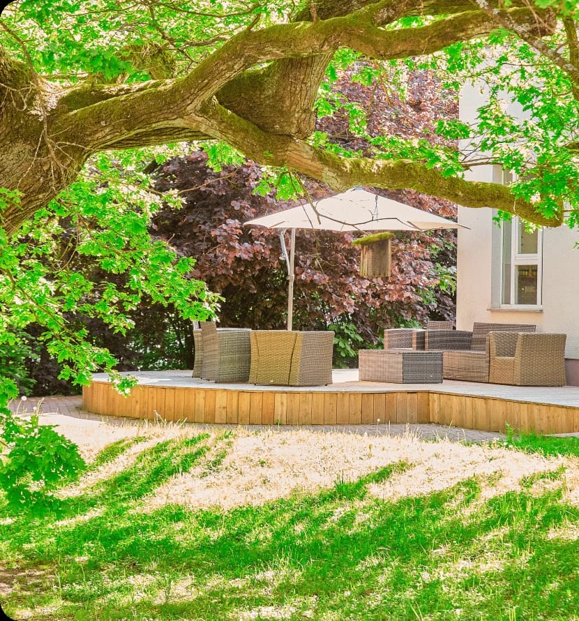 Gartenterrasse mit Loungemöbeln und Sonnenschirm unter einem großen Baum