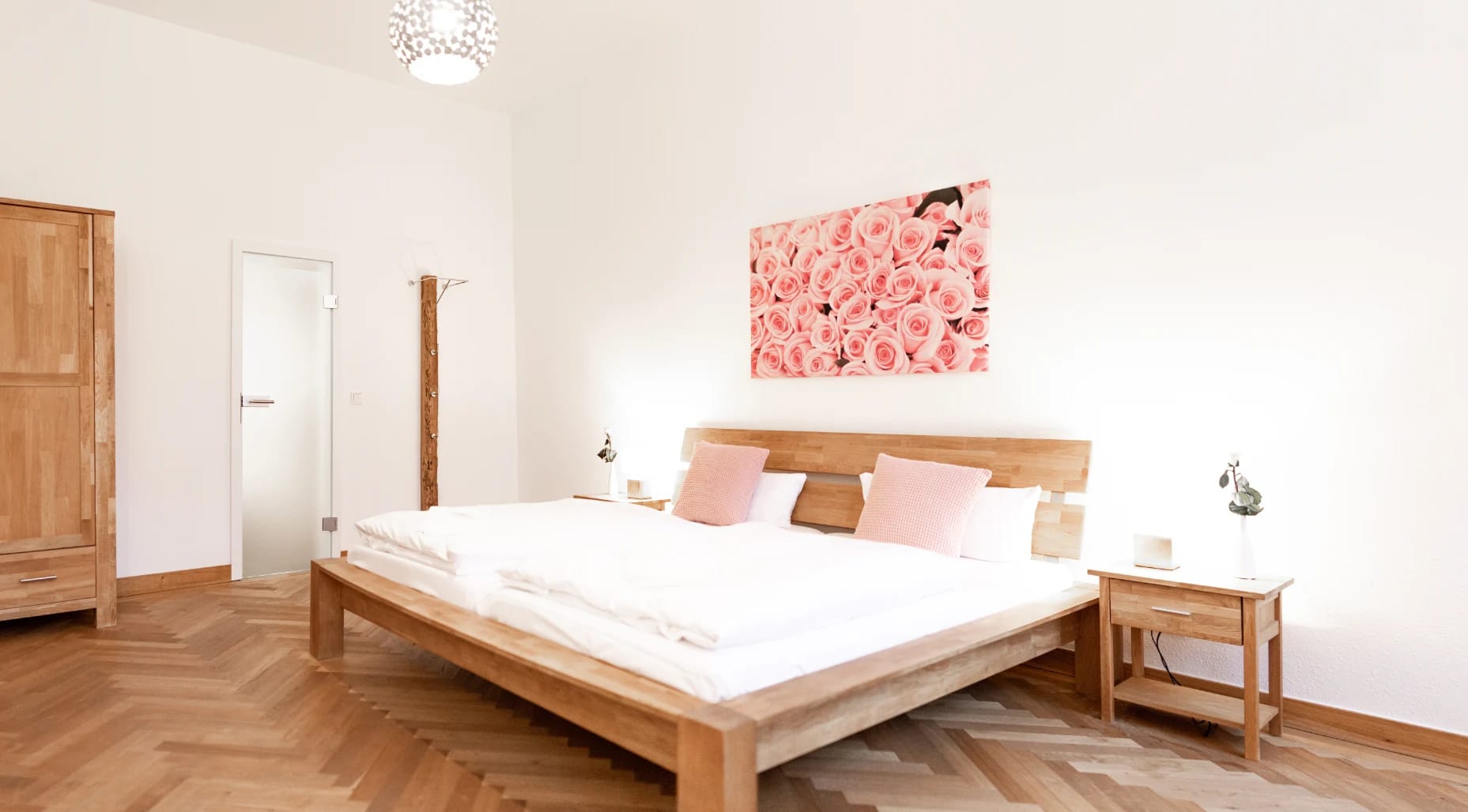 Zimmer mit Holzbett, Kleiderschrank und Rosenbild über dem Kopfende auf Fischgrätparkett