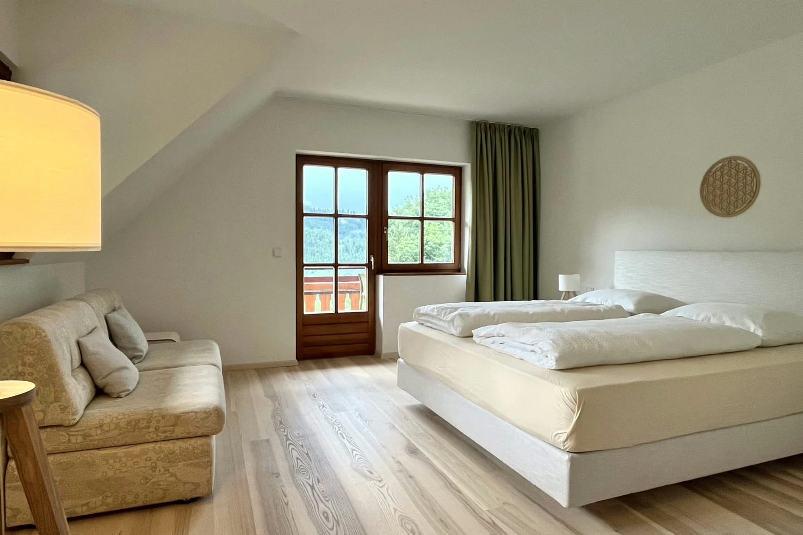 Suite in Naturtönen mit Doppelbett, Polstersofa, hellem Holzboden und Balkontür unter der Dachschräge