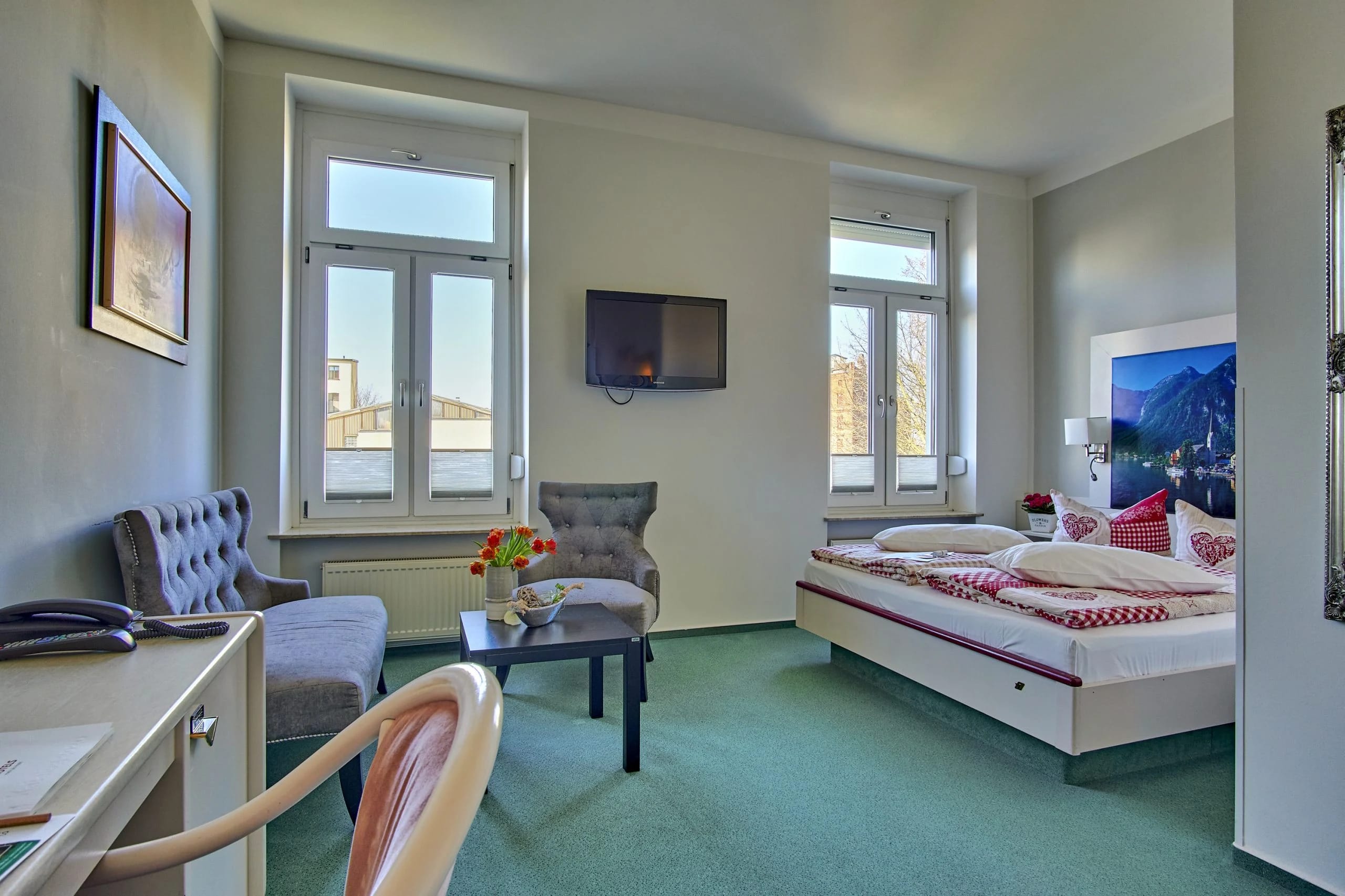 Geräumiges Zimmer mit Sitzecke aus Sesseln, Schreibtisch und Doppelbett vor drei Fenstern