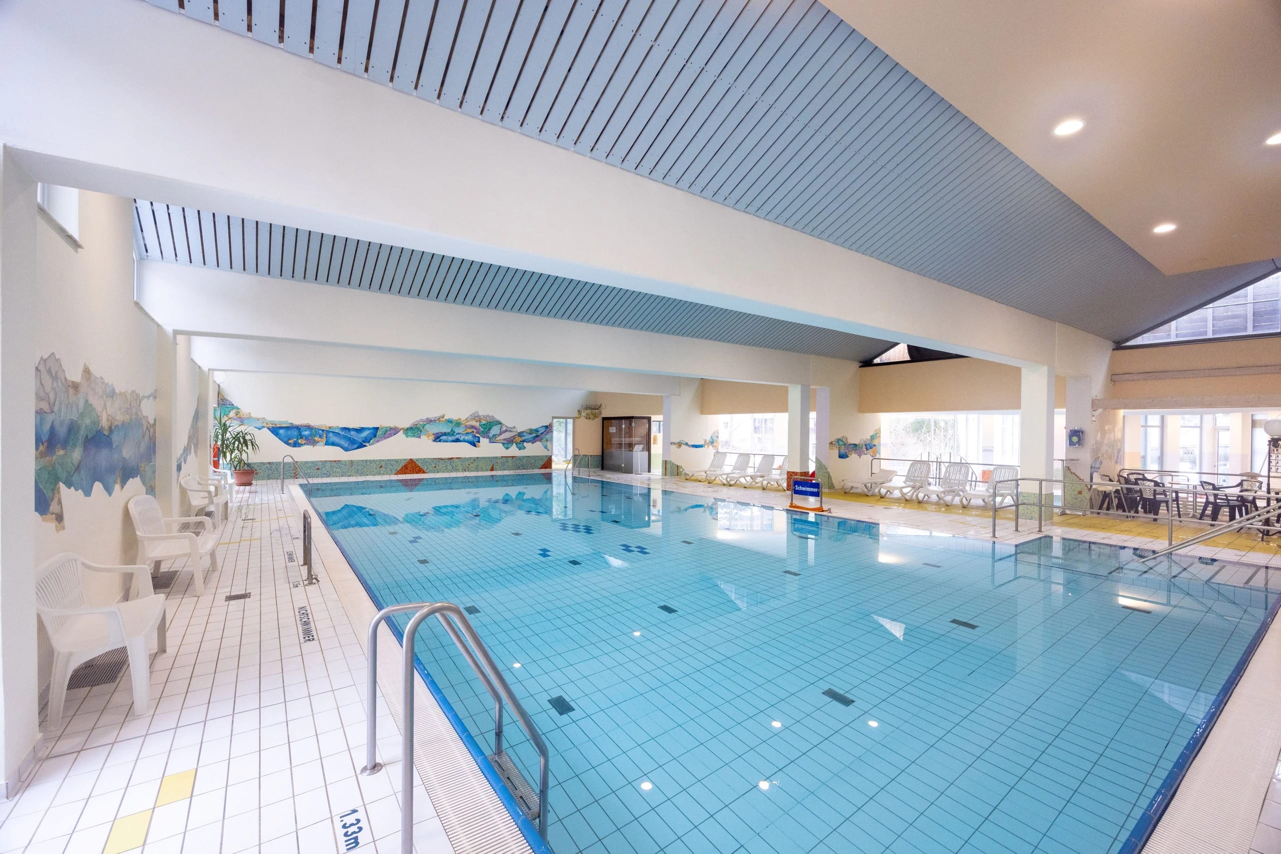 Hallenbad Juramar mit großem Schwimmbecken, Beckentreppe und weißen Stühlen am Beckenrand