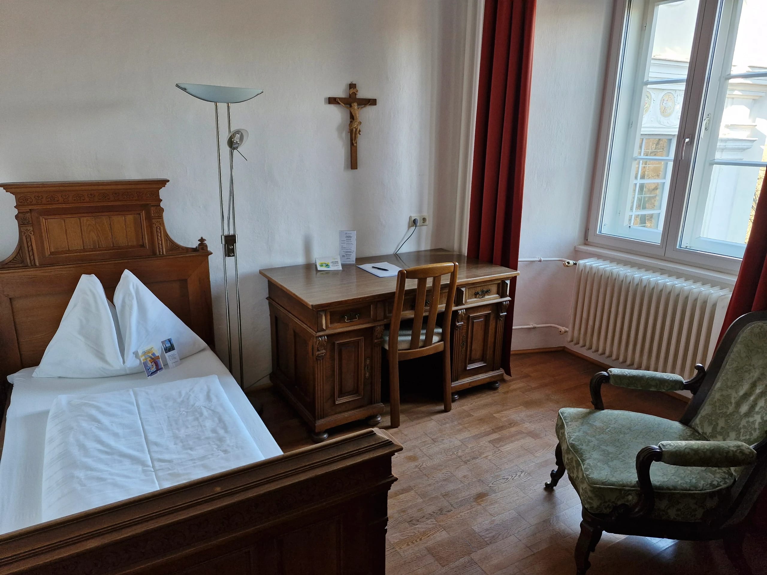 Komfortzimmer mit antikem Holzbett, Schreibtisch und zwei Polstersesseln am Fenster