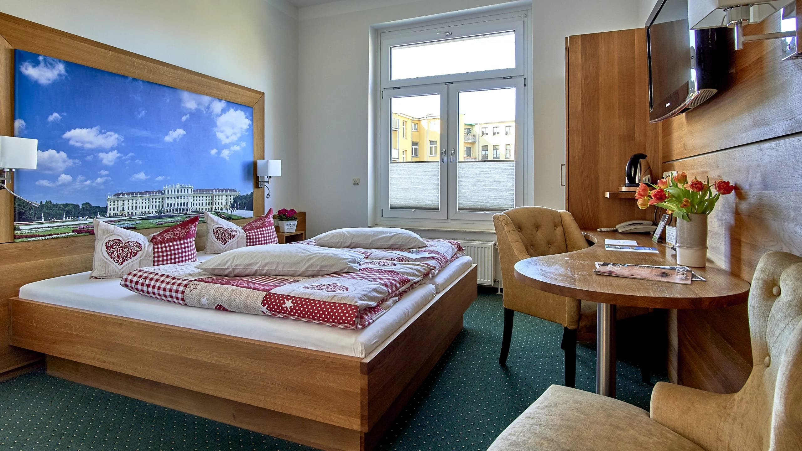 Zimmer mit Doppelbett, rot-weißer Bettwäsche, rundem Holztisch mit Tulpen und Fenster