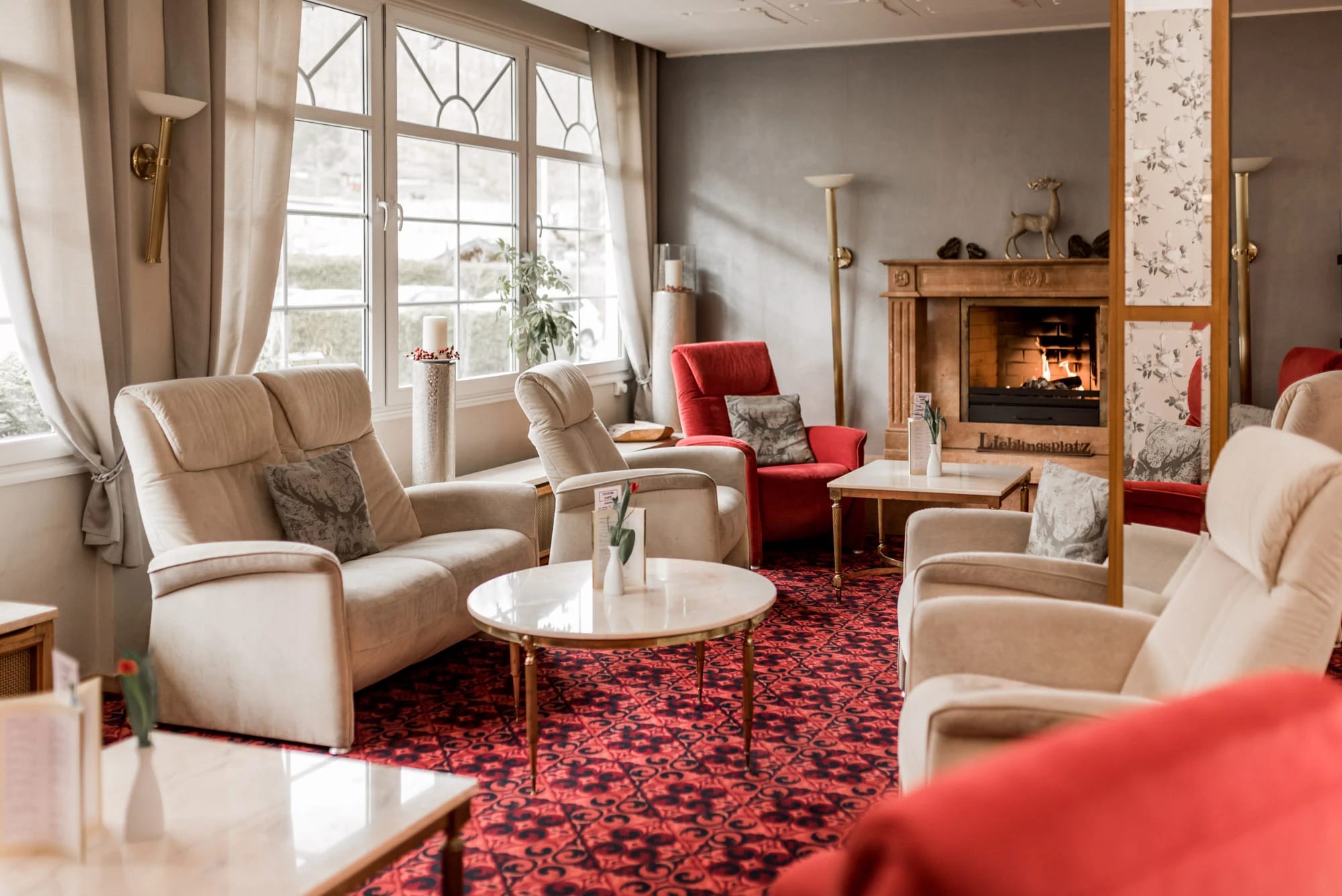 Hotellounge mit offenem Kamin, hellen Polstersesseln und rotem Teppich