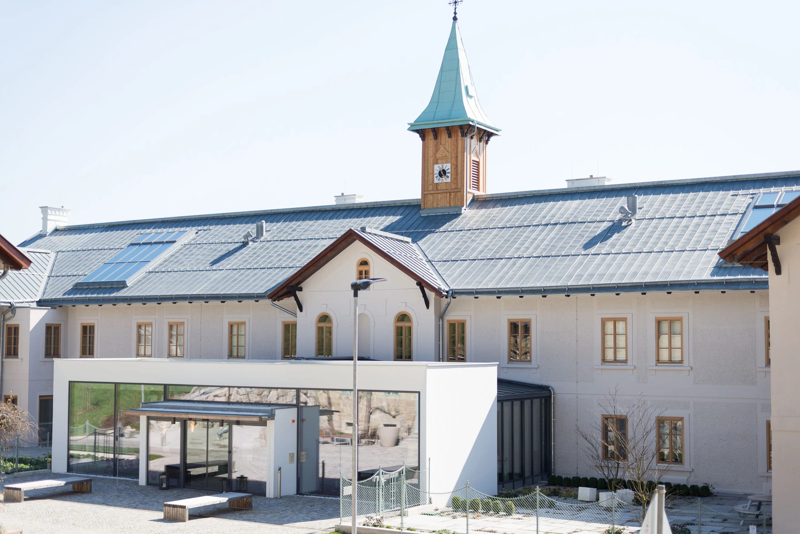 Vorderansicht des weißen Haupthauses mit Turm, verglastem Eingangspavillon und Vorplatz