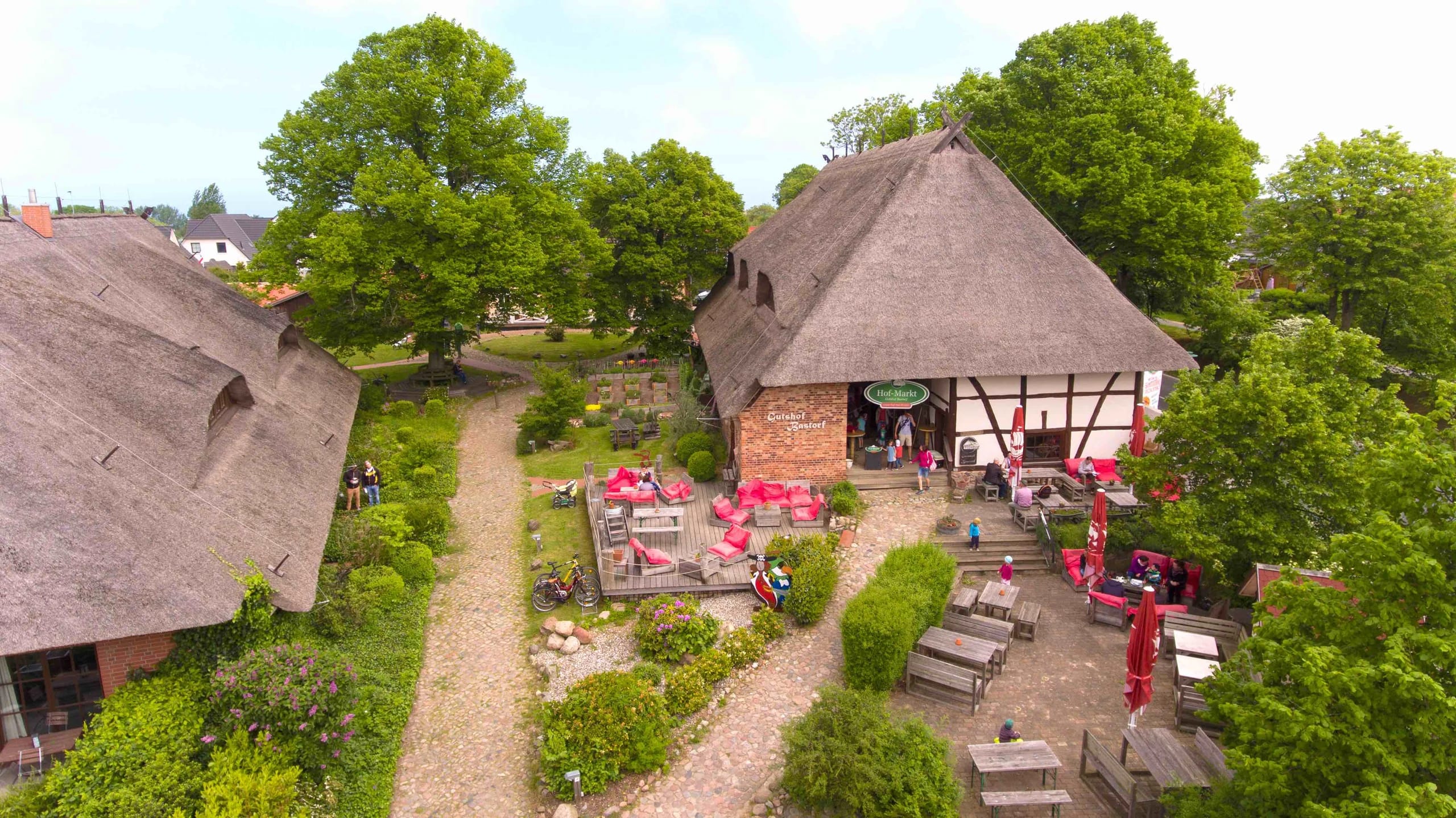 Luftaufnahme des Gutshofs mit reetgedeckten Häusern, Innenhof und altem Baumbestand