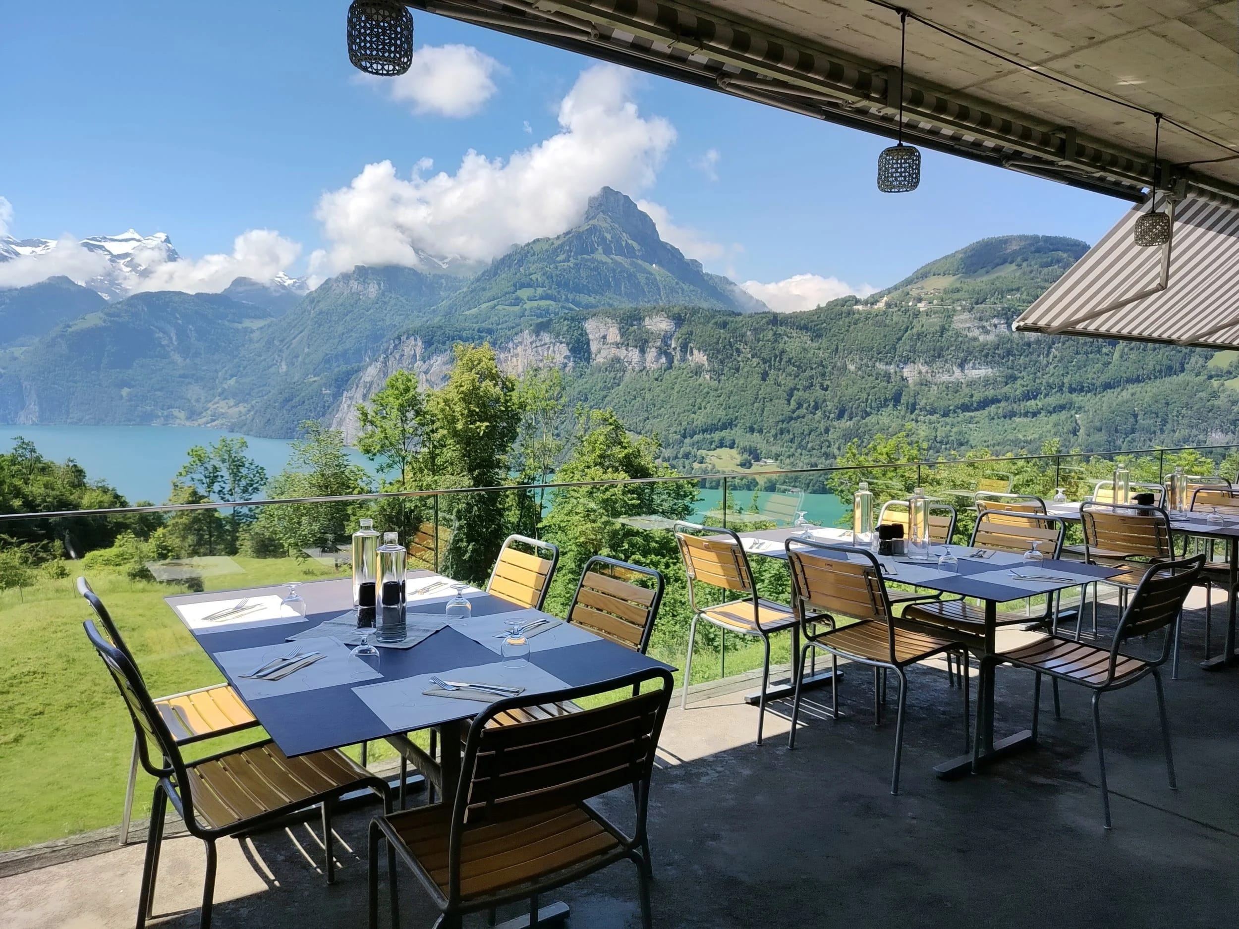 Gedeckte Terrasse mit Holzstühlen und Blick auf See und Berge
