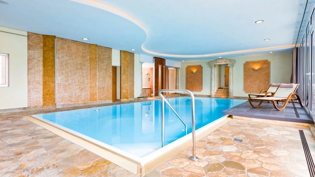 Hallenbad mit blauem Becken, Natursteinboden und zwei Holzliegen am Beckenrand