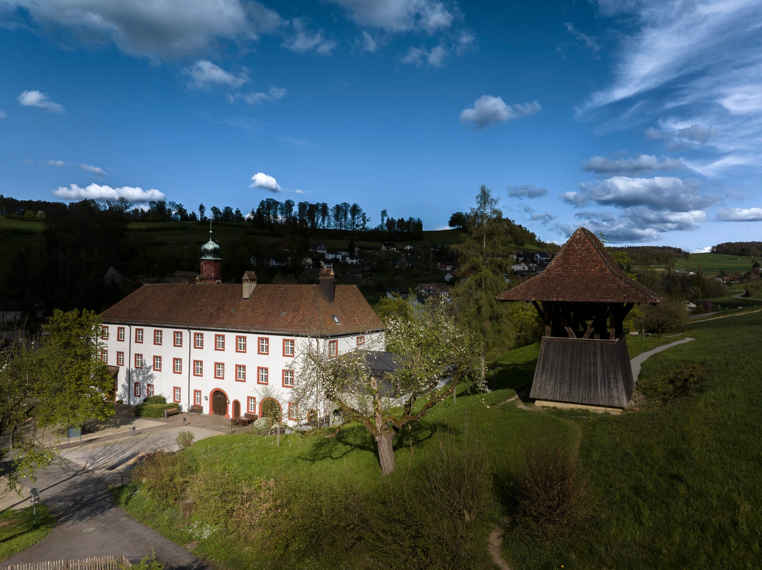 Hauptgebäude mit dem historischen hölzernen Glockenturm auf der angrenzenden Wiese