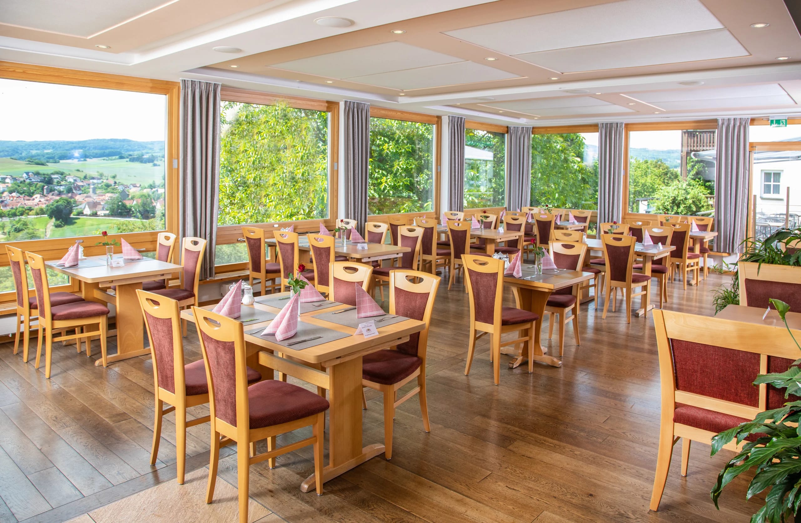 Panoramarestaurant mit Holztischen, Stoffservietten und umlaufender Fensterfront ins Grüne
