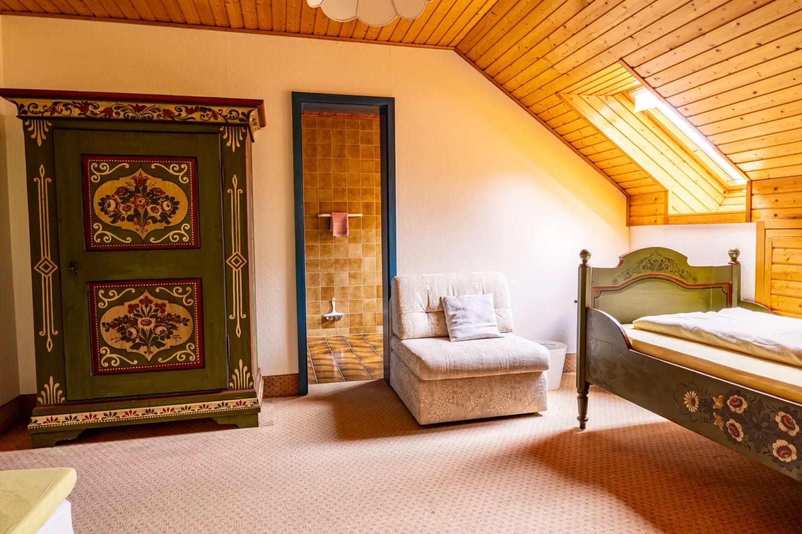 Zimmer mit Holzdecke, bemaltem Bauernschrank, bemaltem Einzelbett und gepolstertem Sessel