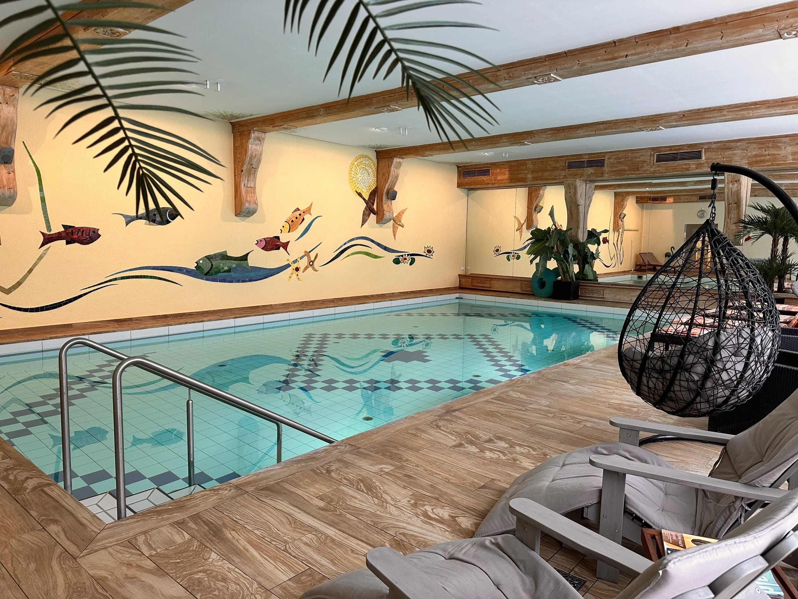 Hallenbad mit Fischmalerei an der Wand, Hängesessel und Liegen am Beckenrand