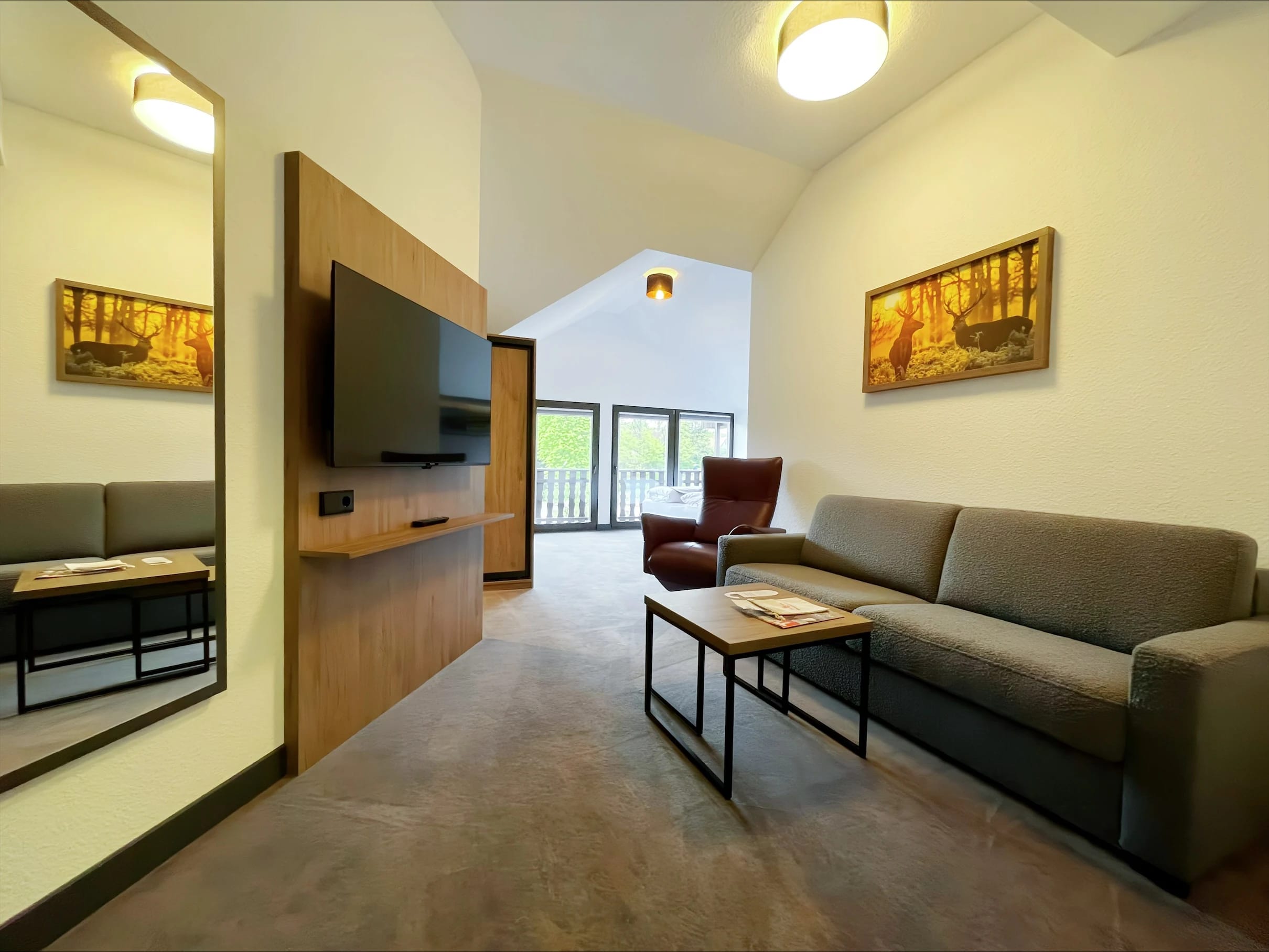 Wohnbereich mit Sofa, Sessel, Couchtisch und Fernseher an einer Holzwand